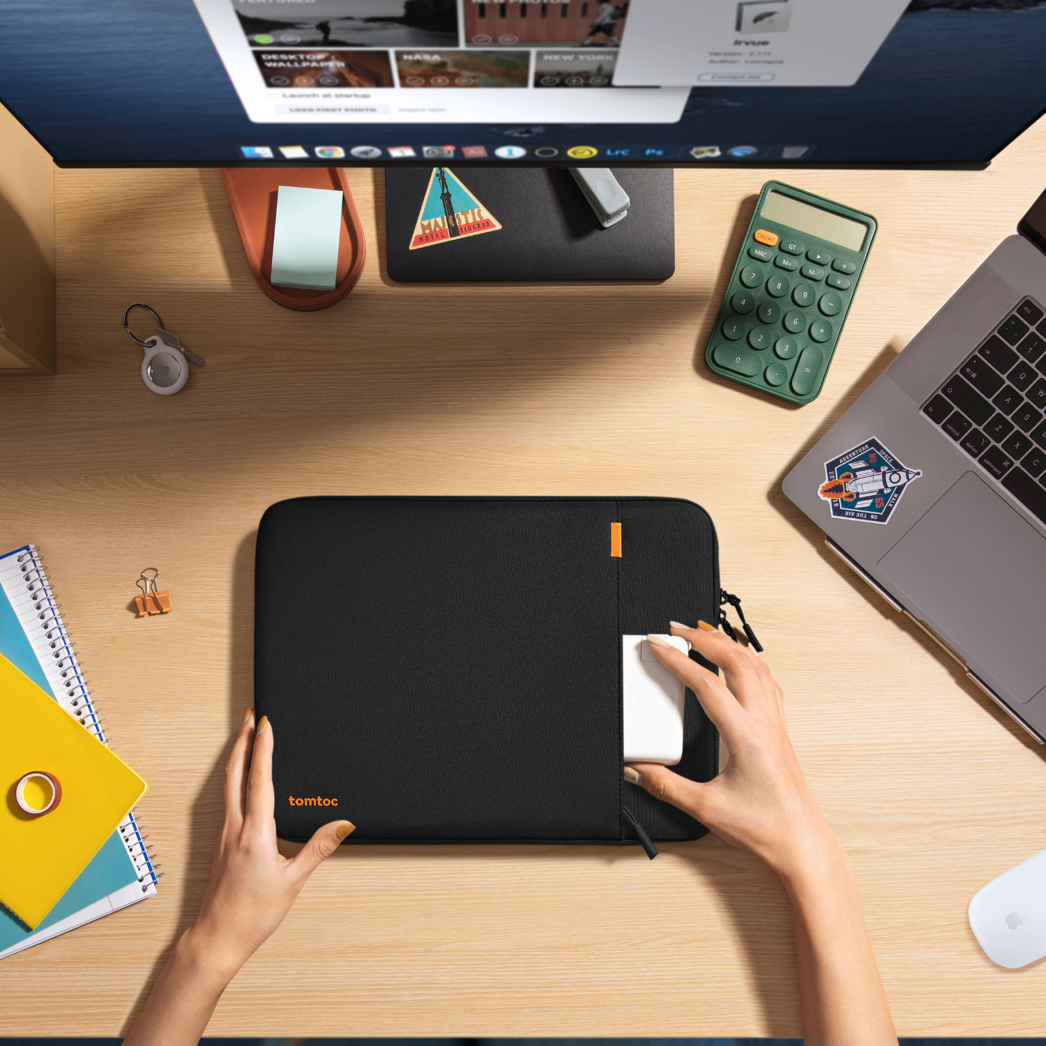 Ręce wkładają białą ładowarkę do czarnego etui tomtoc na drewnianym biurku z komputerem i akcesoriami.