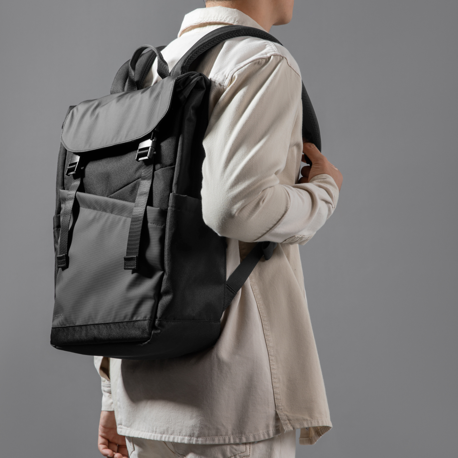 Uomo con zaino nero e grigio, vista laterale, sfondo grigio.