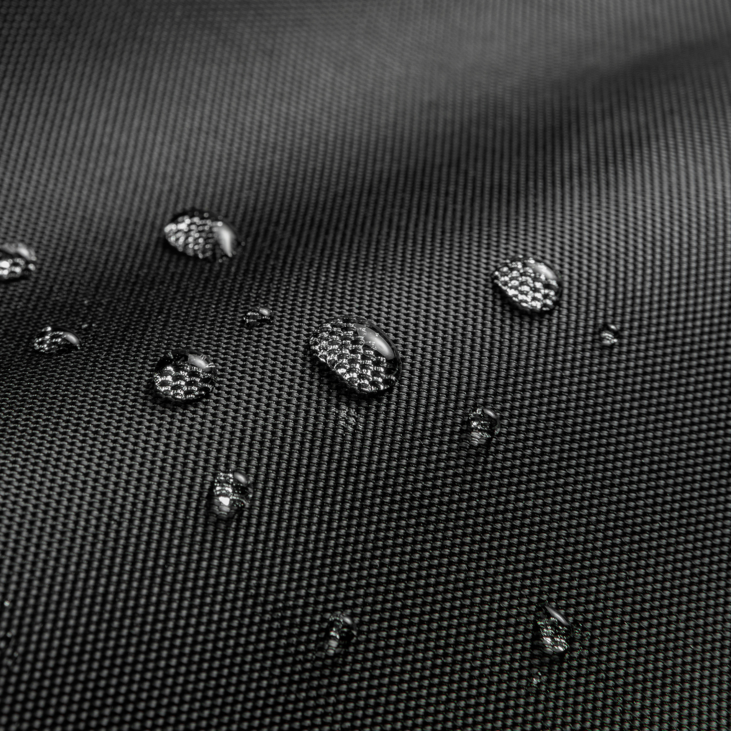 Zbliżenie kropli wody na czarnej, teksturowanej powierzchni. Krople są przezroczyste i błyszczące.