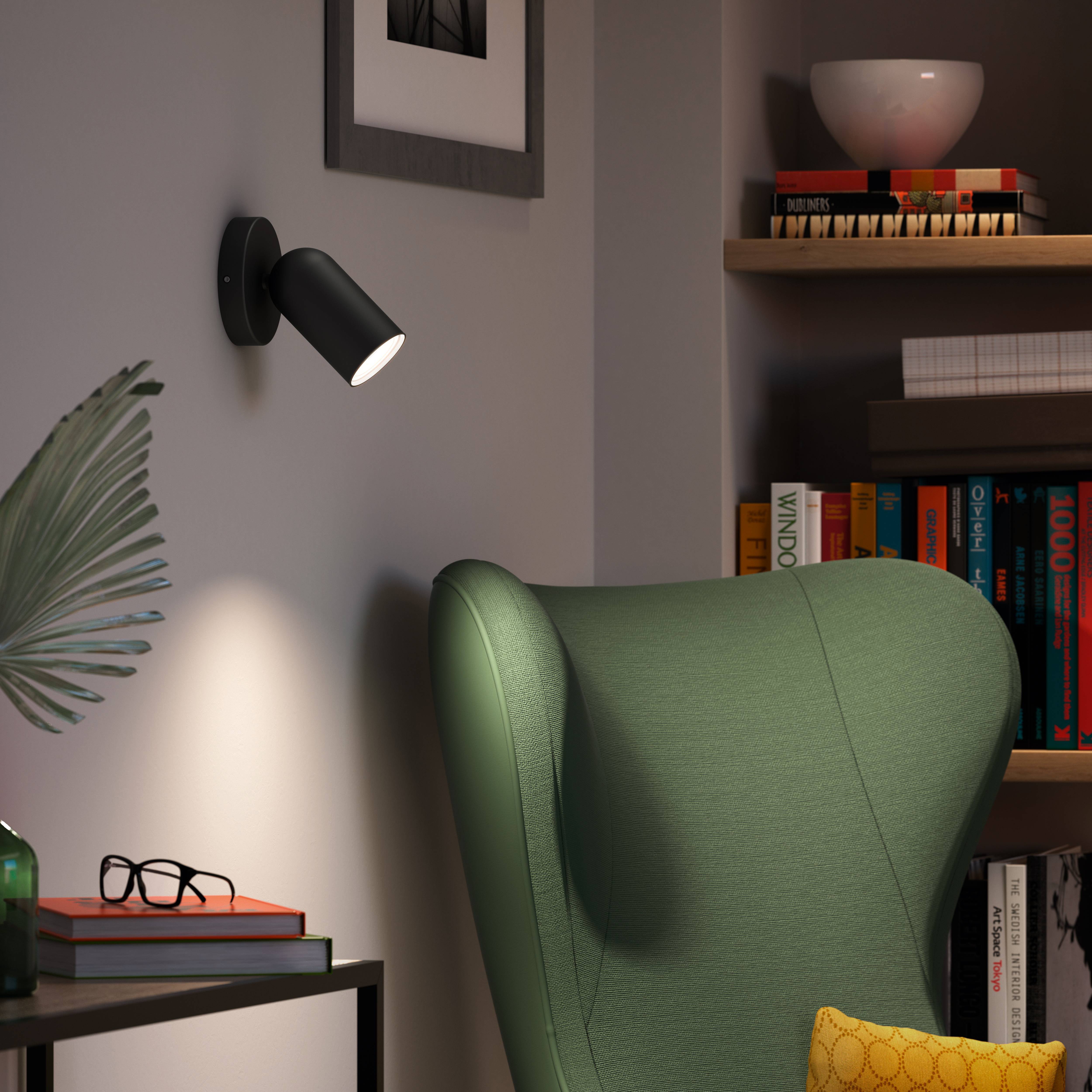 Schwarzer Wandstrahler beleuchtet einen grünen Sessel. Bücherregale im Hintergrund.