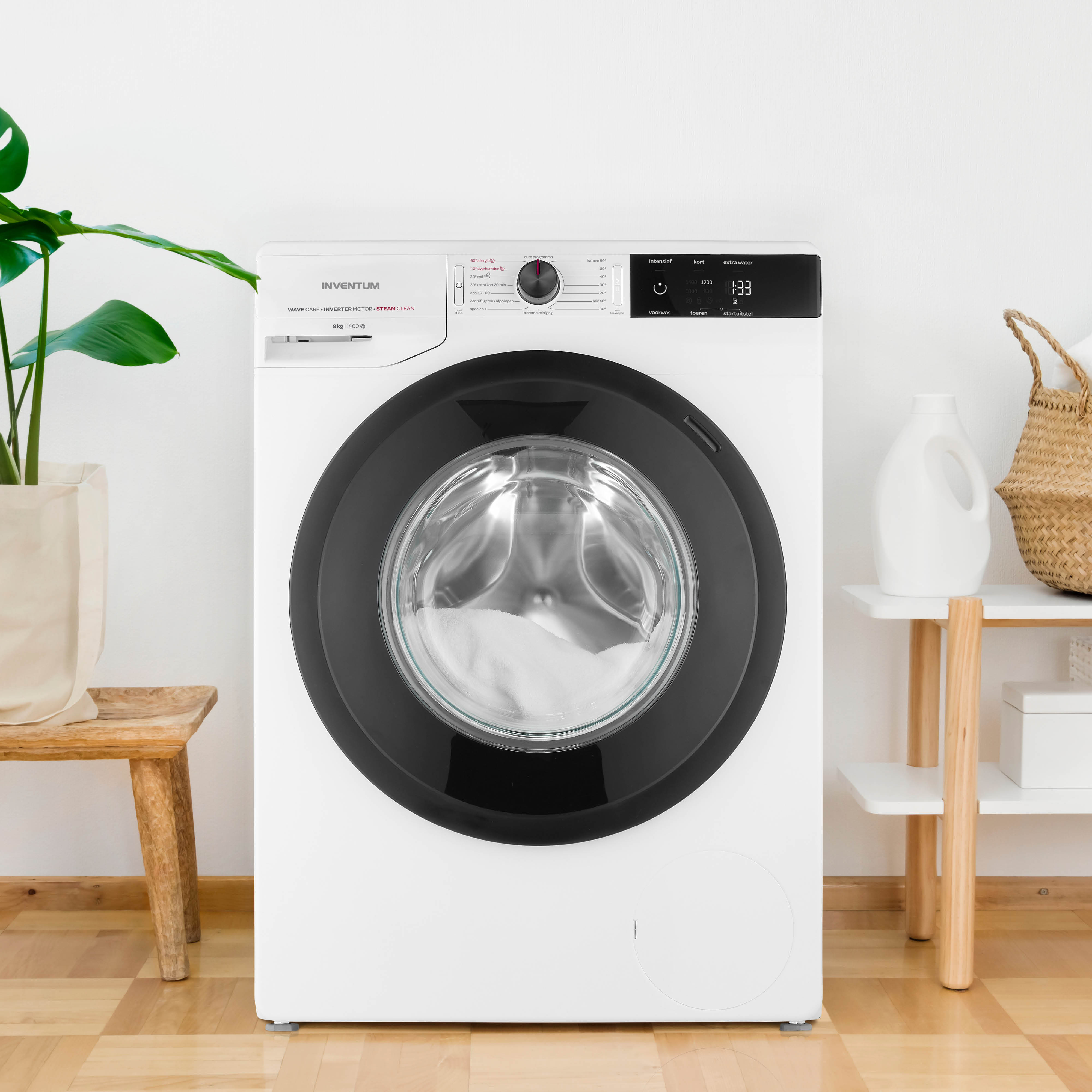 Witte wasmachine met zwarte deur. Houten krukje en plant links, planken met items rechts.