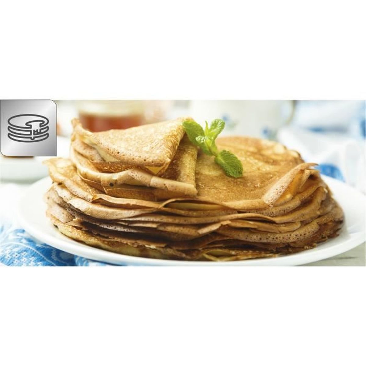 Una pila di crêpes su un piatto, con foglie di menta e un bicchiere di sciroppo su sfondo bianco.