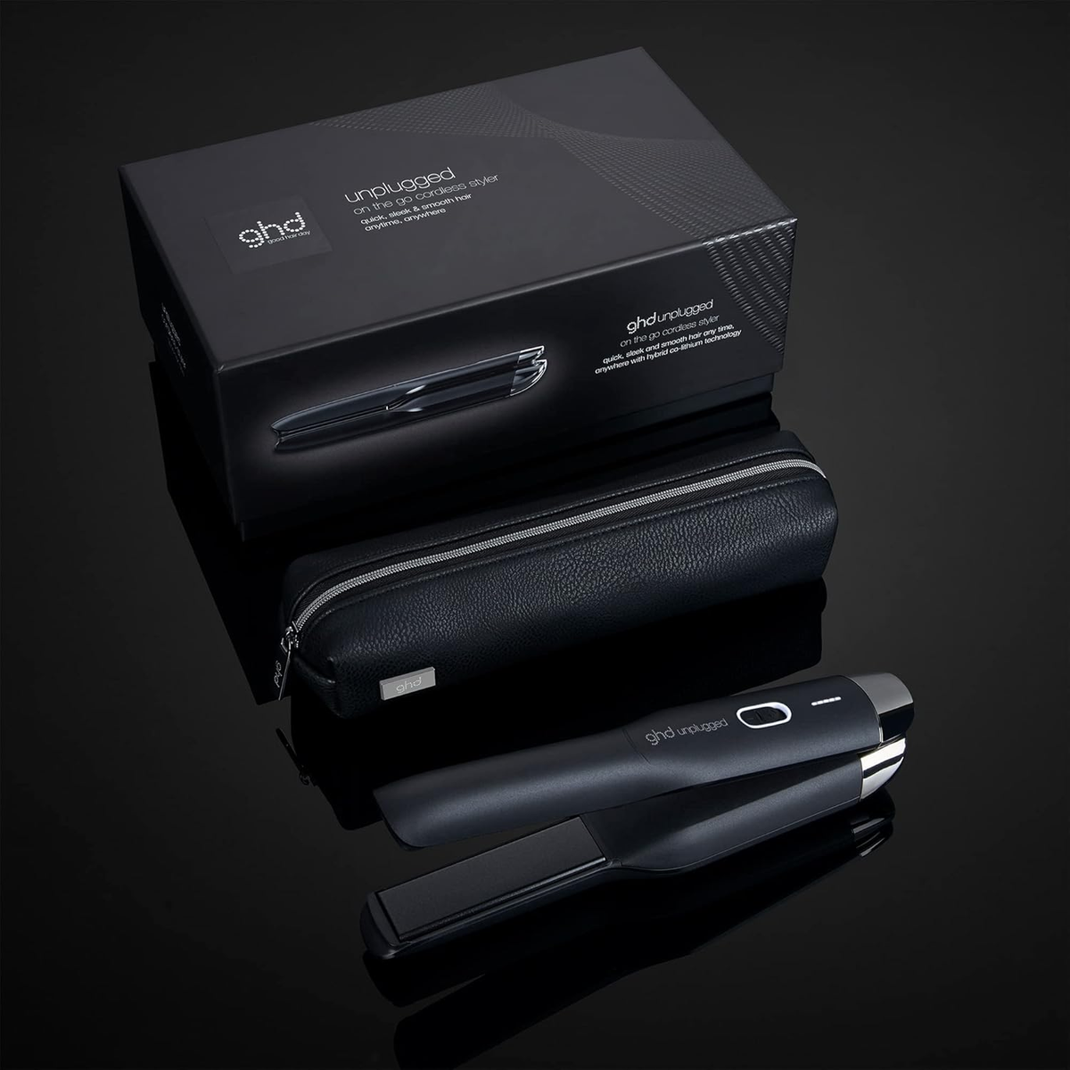 Schwarzes ghd Unplugged Glätteisen, Schachtel und Etui auf einer reflektierenden schwarzen Oberfläche.