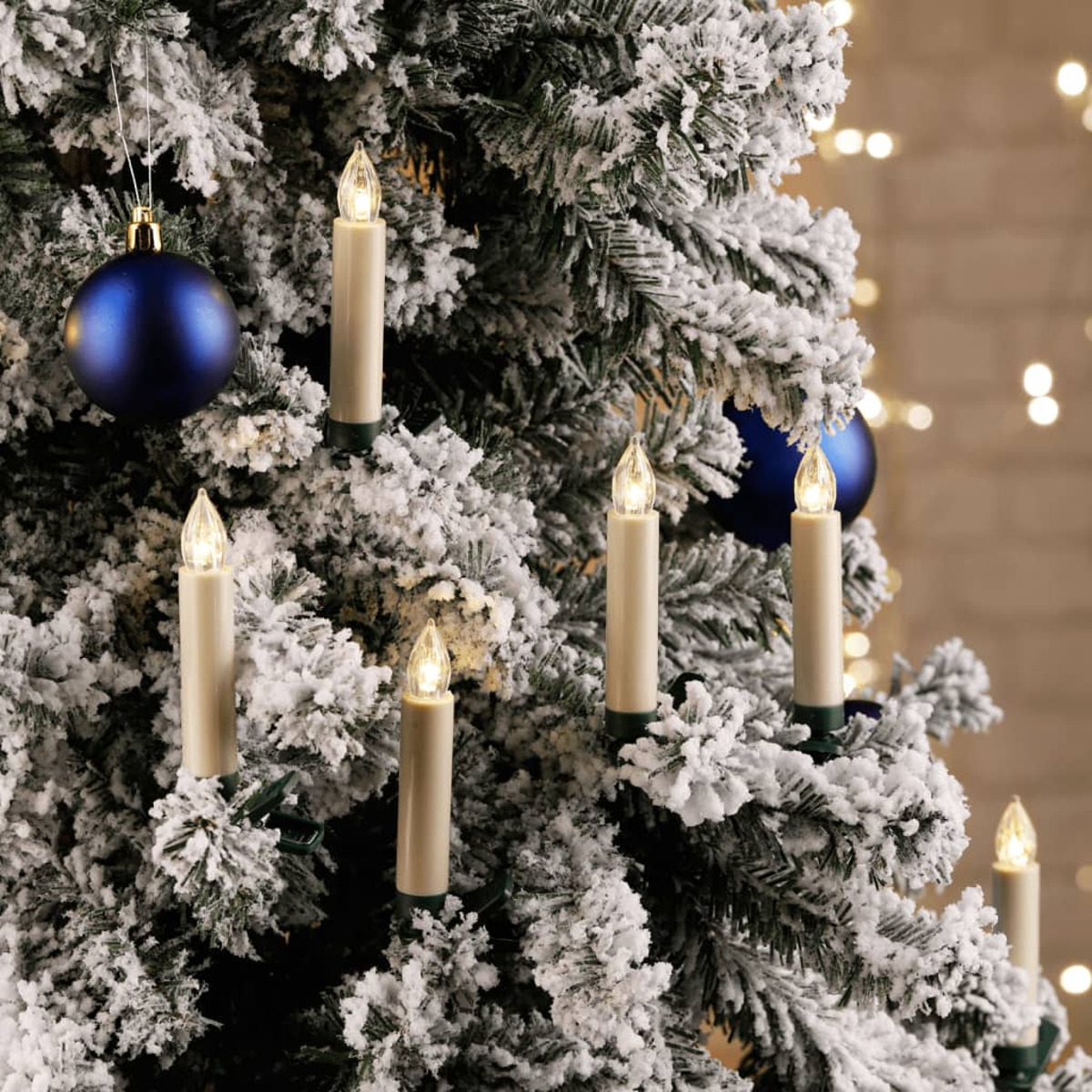 Schneebedeckter Weihnachtsbaum mit Kerzenlichtern und blauen Ornamenten. Der Hintergrund ist verschwommen.