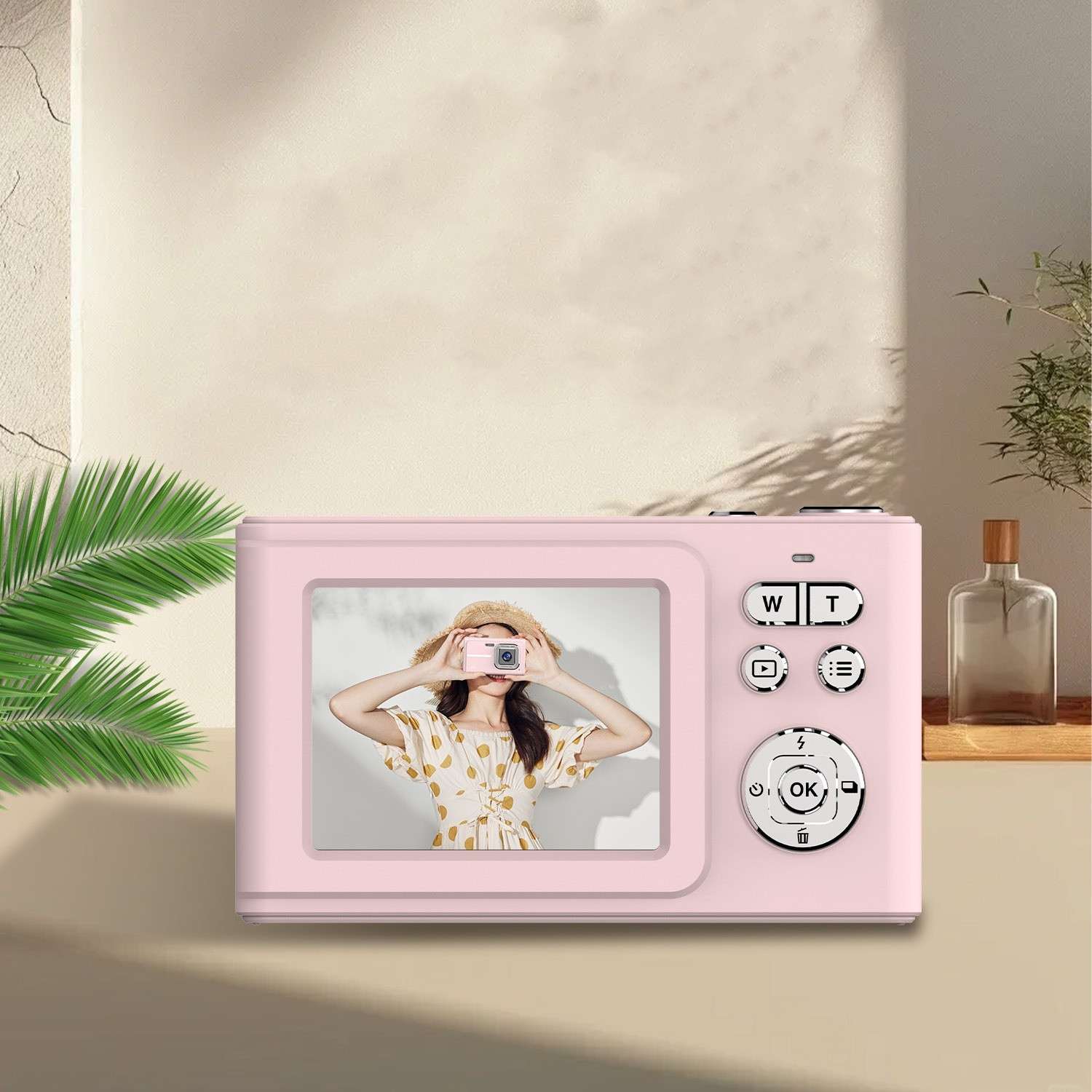 Eine pinke Digitalkamera, die eine Frau hält. Hintergrund ist eine hellbraune Wand mit Pflanzen.