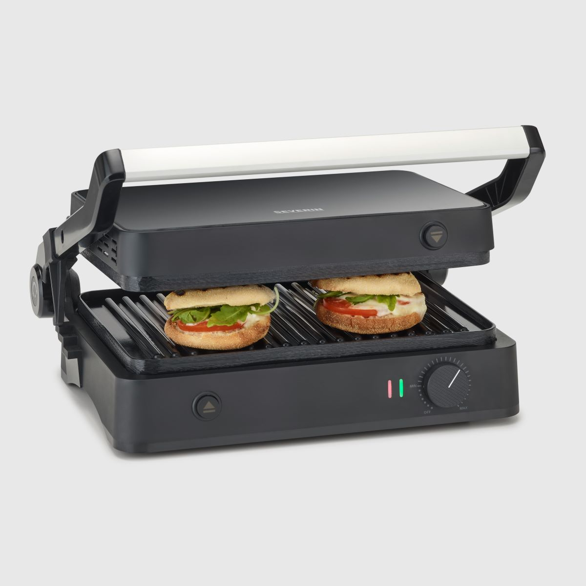 A black panini press with two sandwiches inside. The sandwiches have bread, tomato, and leafy greens.