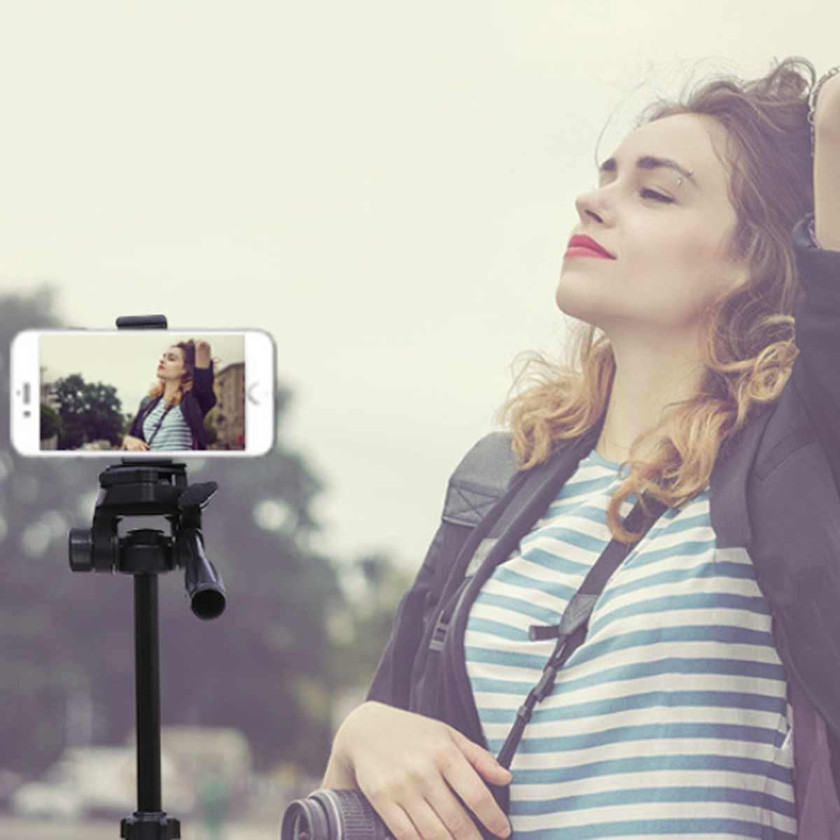 Eine Frau macht ein Foto mit einem Smartphone auf einem Stativ. Der Hintergrund sind verschwommene Bäume und Himmel.