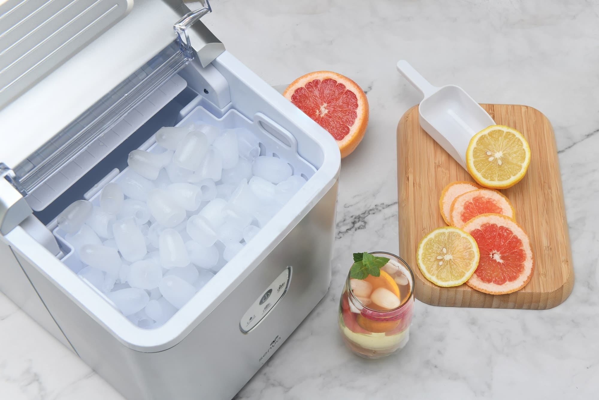 Eismaschine mit Eiswürfeln und etwas Obst. Es gibt ein Glas mit Obst. Der Hintergrund ist weiß.