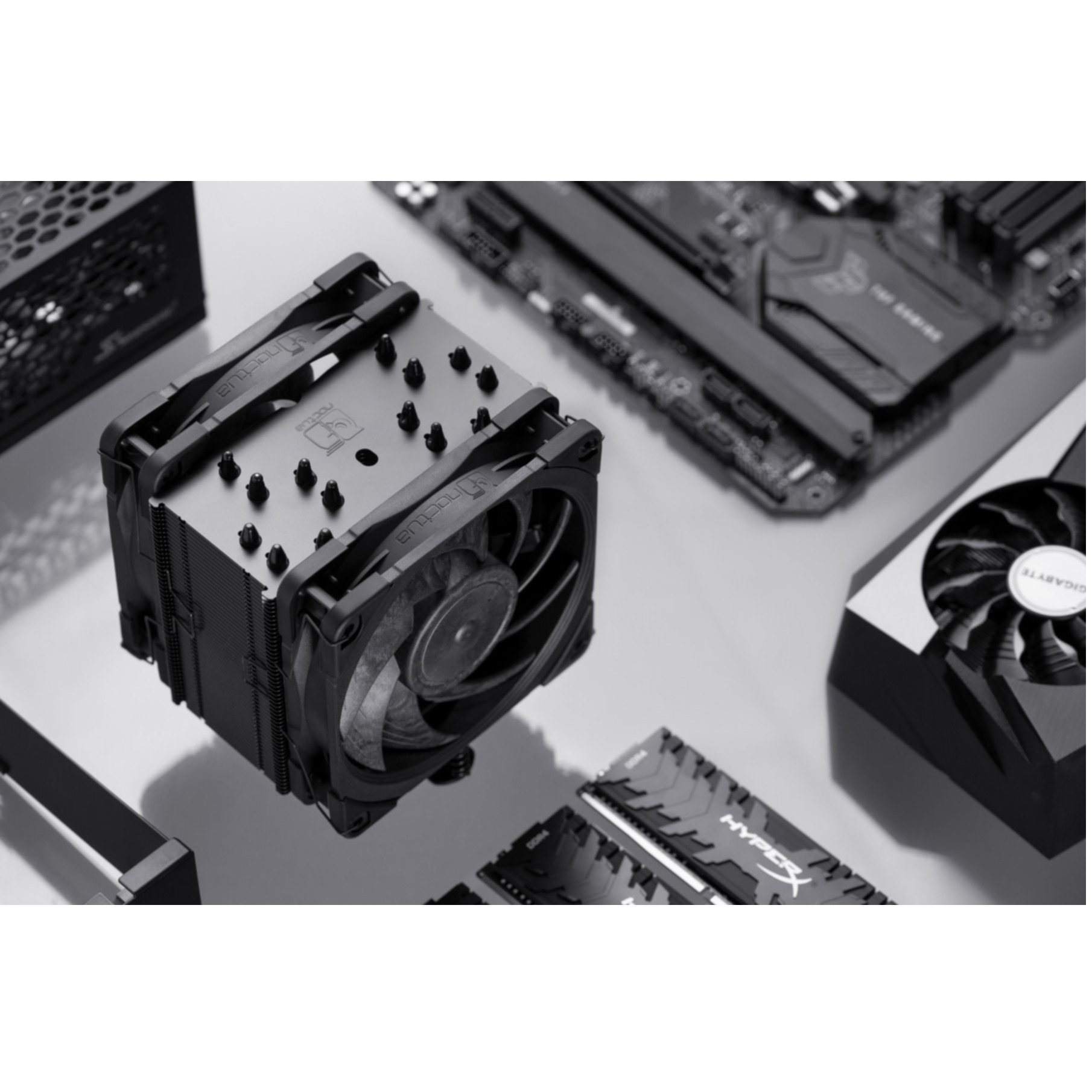 Podzespoły komputera: chłodzenie CPU, RAM, płyta główna i karta graficzna, na szarej powierzchni.