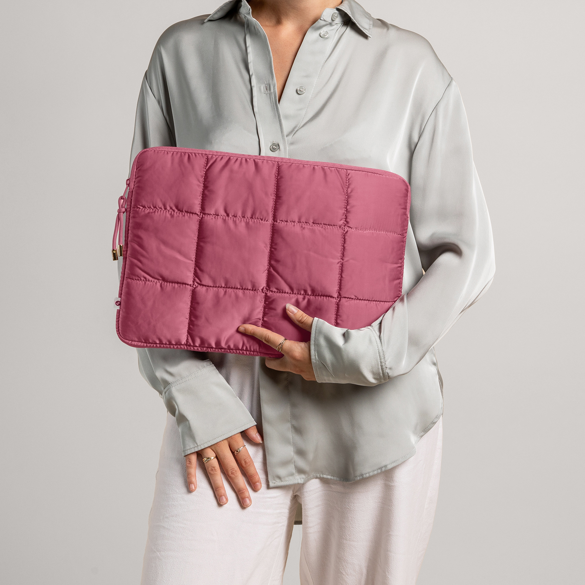 Woman holding a pink quilted laptop case. Light background and clothing.