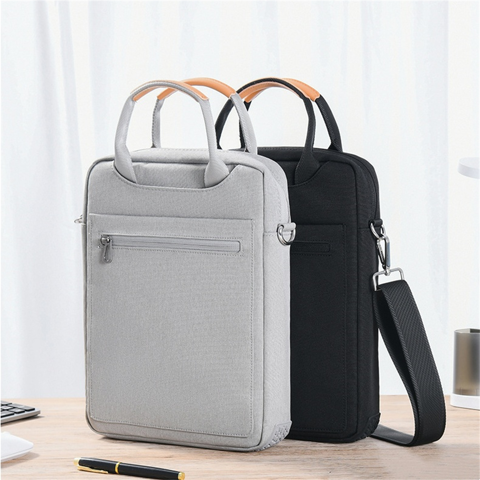 Zwei Laptop-Taschen, grau und schwarz, mit Griffen und Reißverschluss, vor hellem Hintergrund.