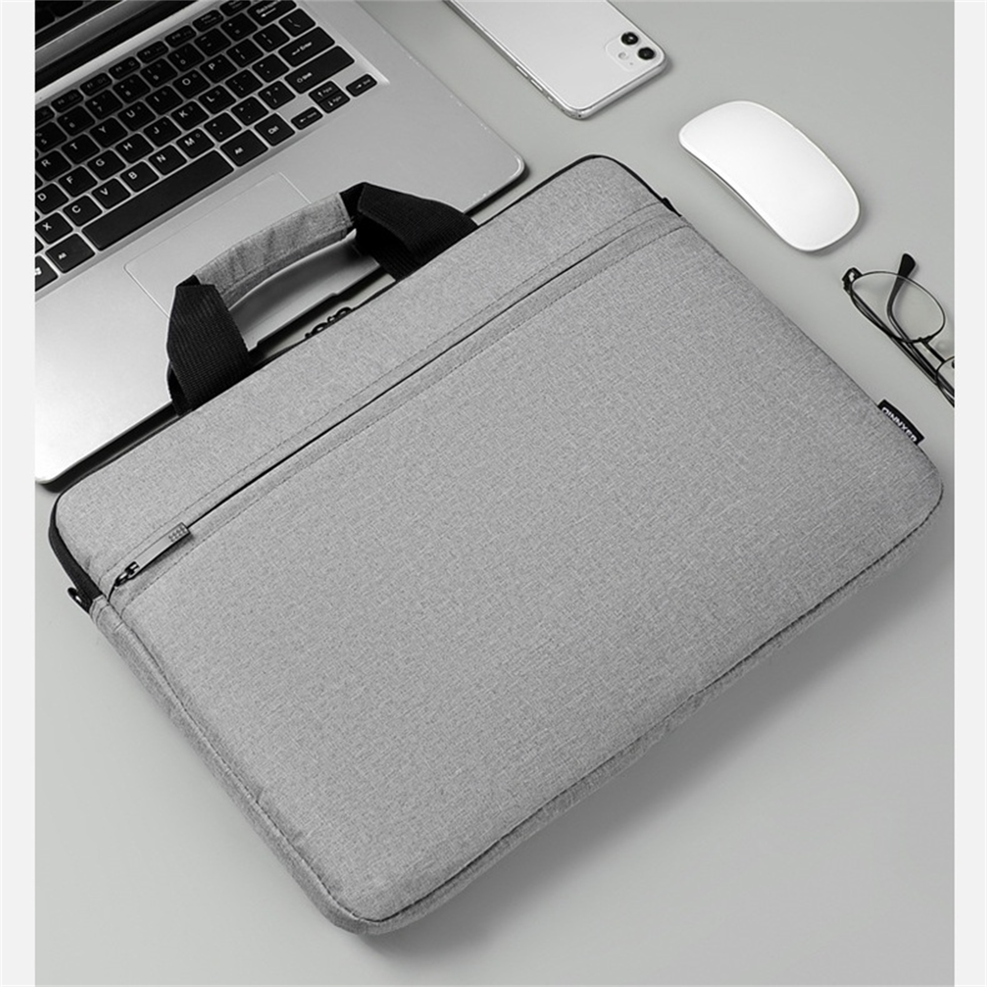 Eine graue Laptoptasche auf einem Schreibtisch, mit Laptop, Telefon, Maus und Brille.