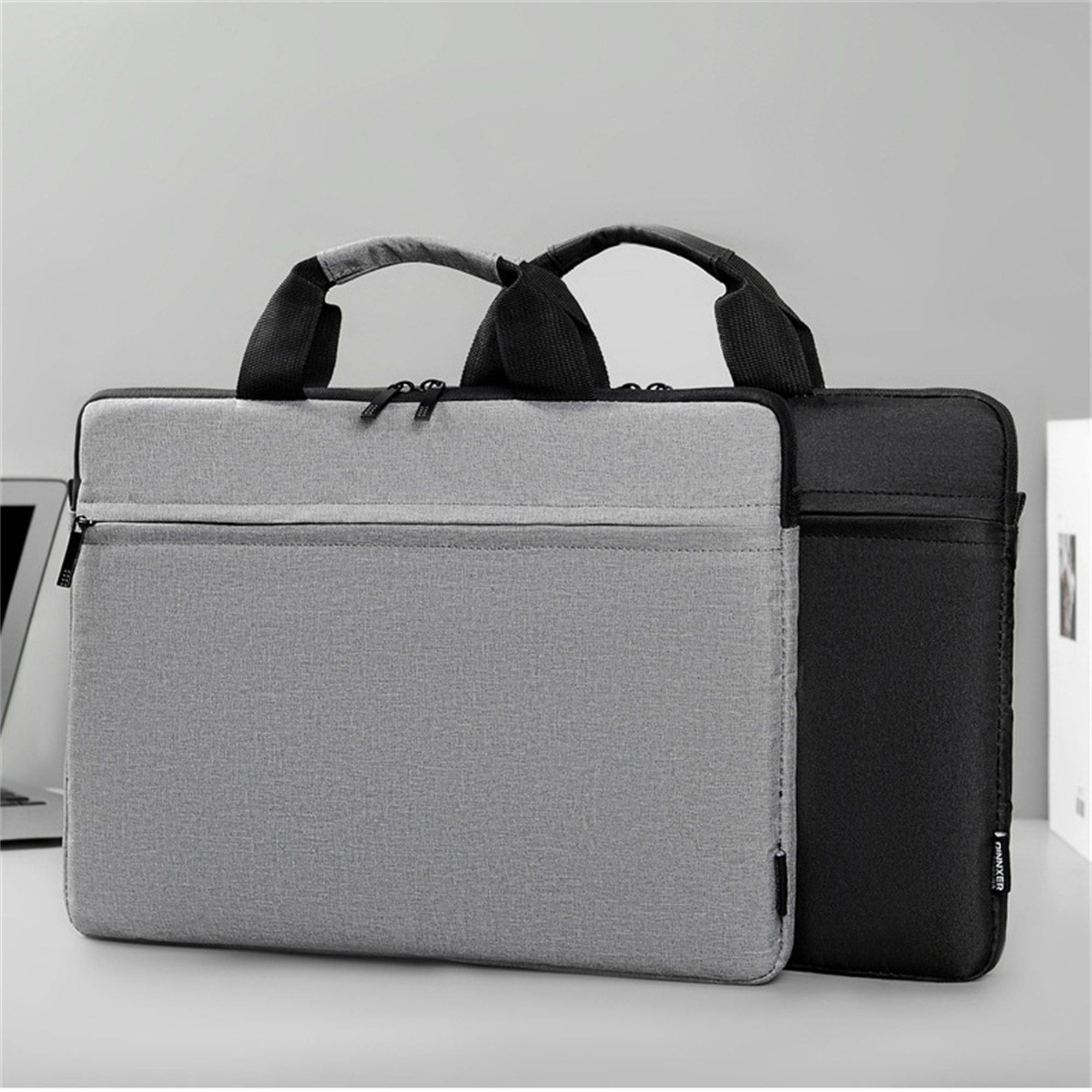 Zwei Laptoptaschen, eine grau, eine schwarz, auf weißer Oberfläche.