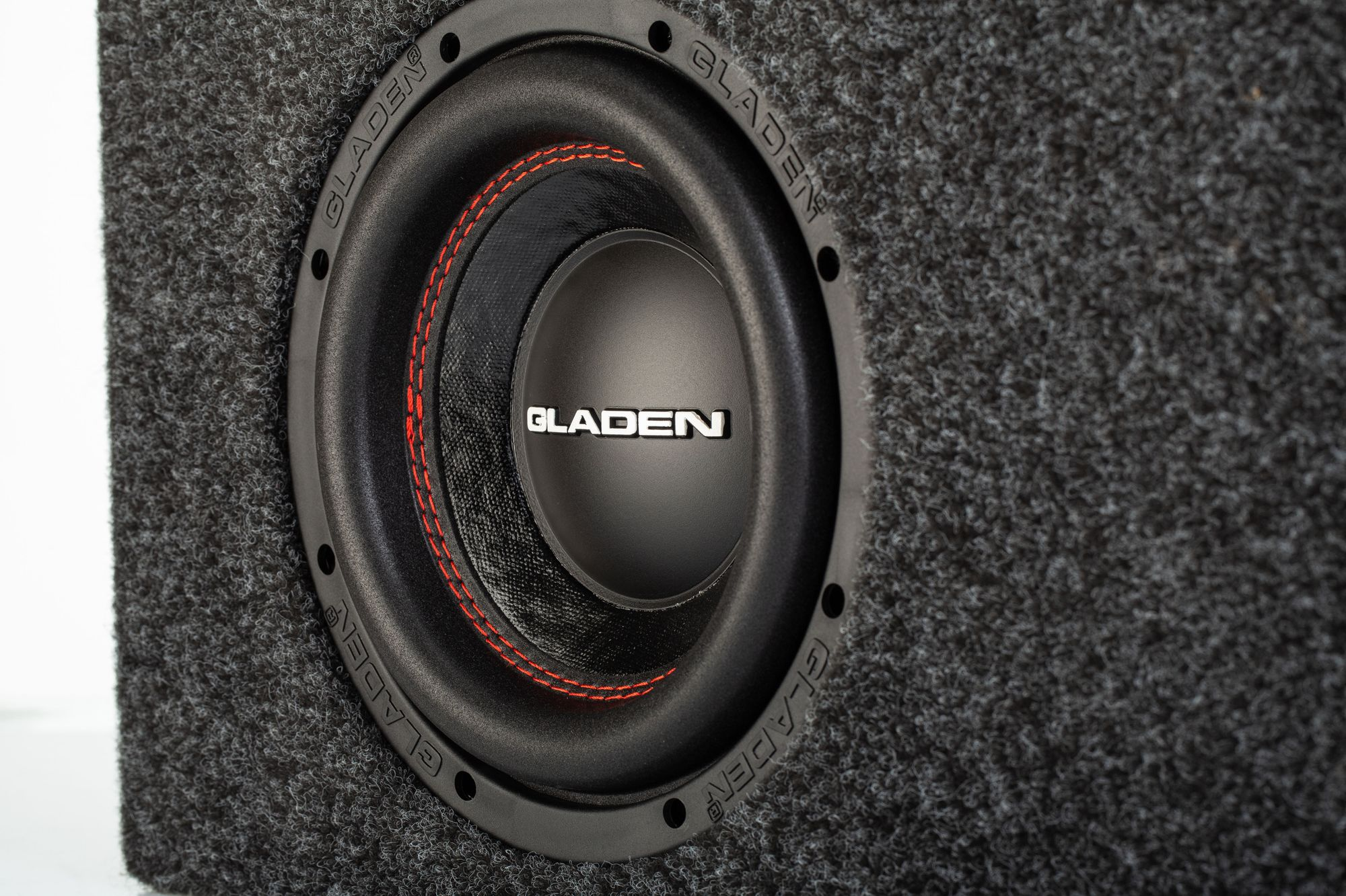 Ein Subwoofer-Lautsprecher mit schwarzem Konus und roten Nähten in einer schwarzen Box.