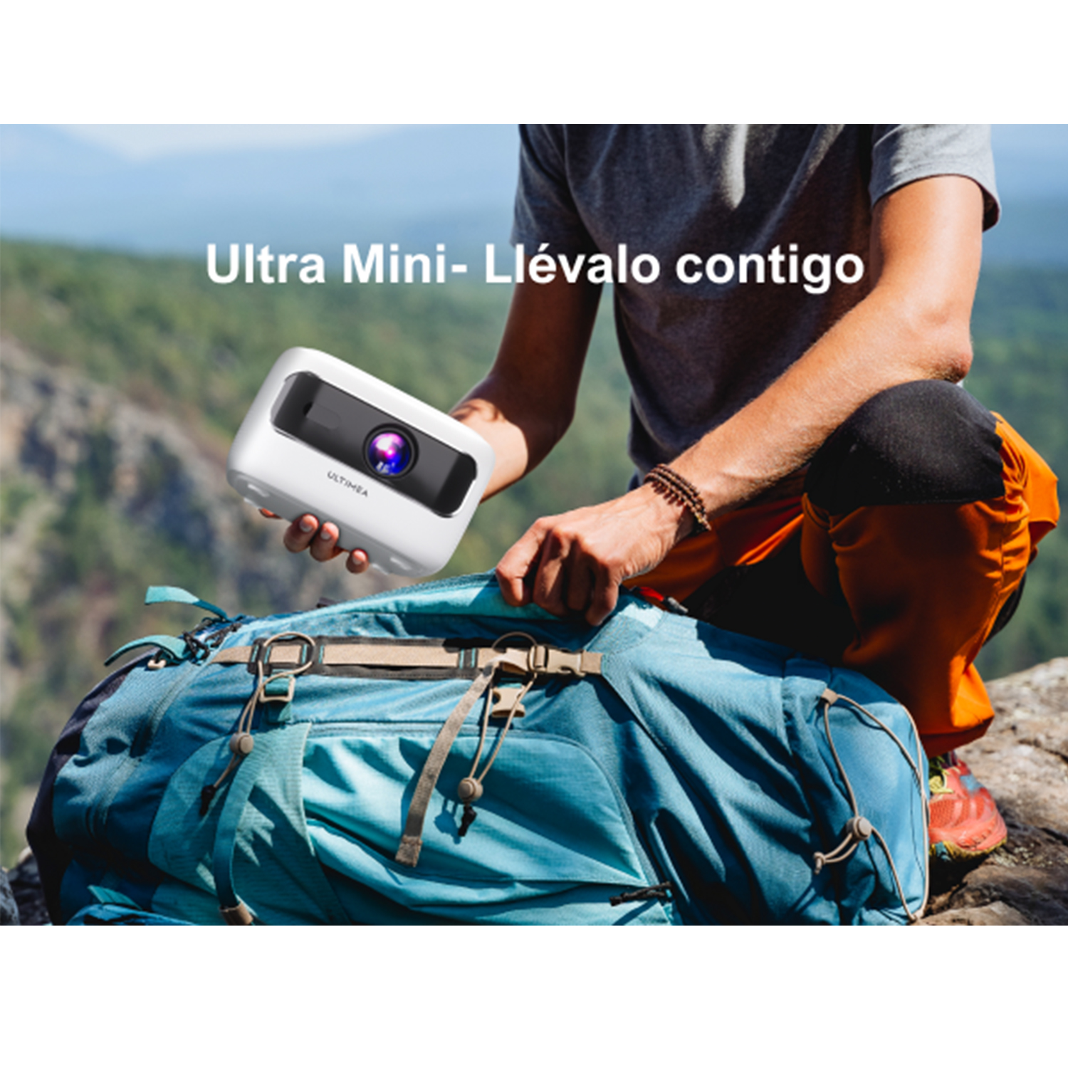 Persona sosteniendo un pequeño proyector blanco cerca de una mochila azul al aire libre.