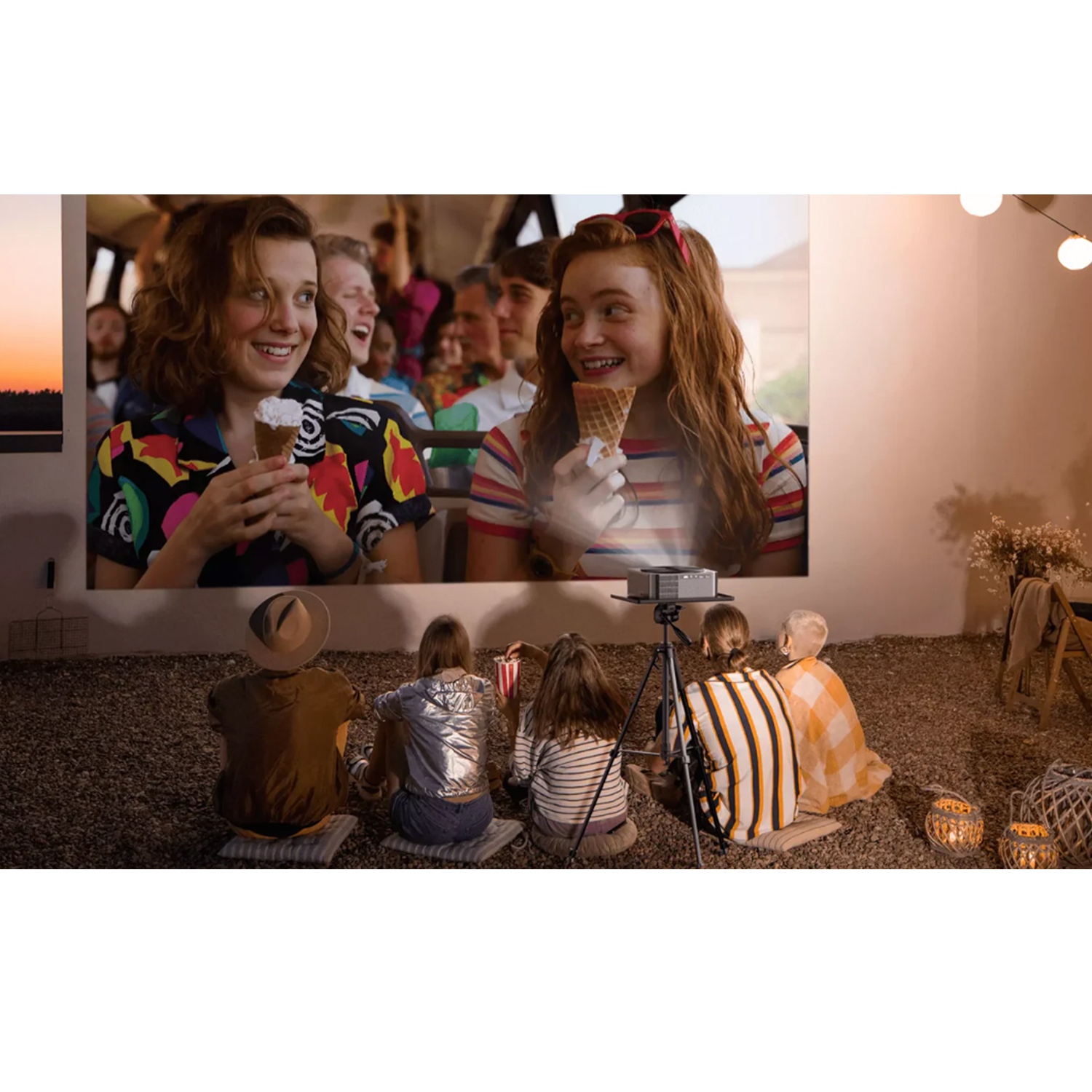 Dzieci oglądają film wyświetlany na ścianie. Dwie dziewczyny z lodami, projektor na statywie.