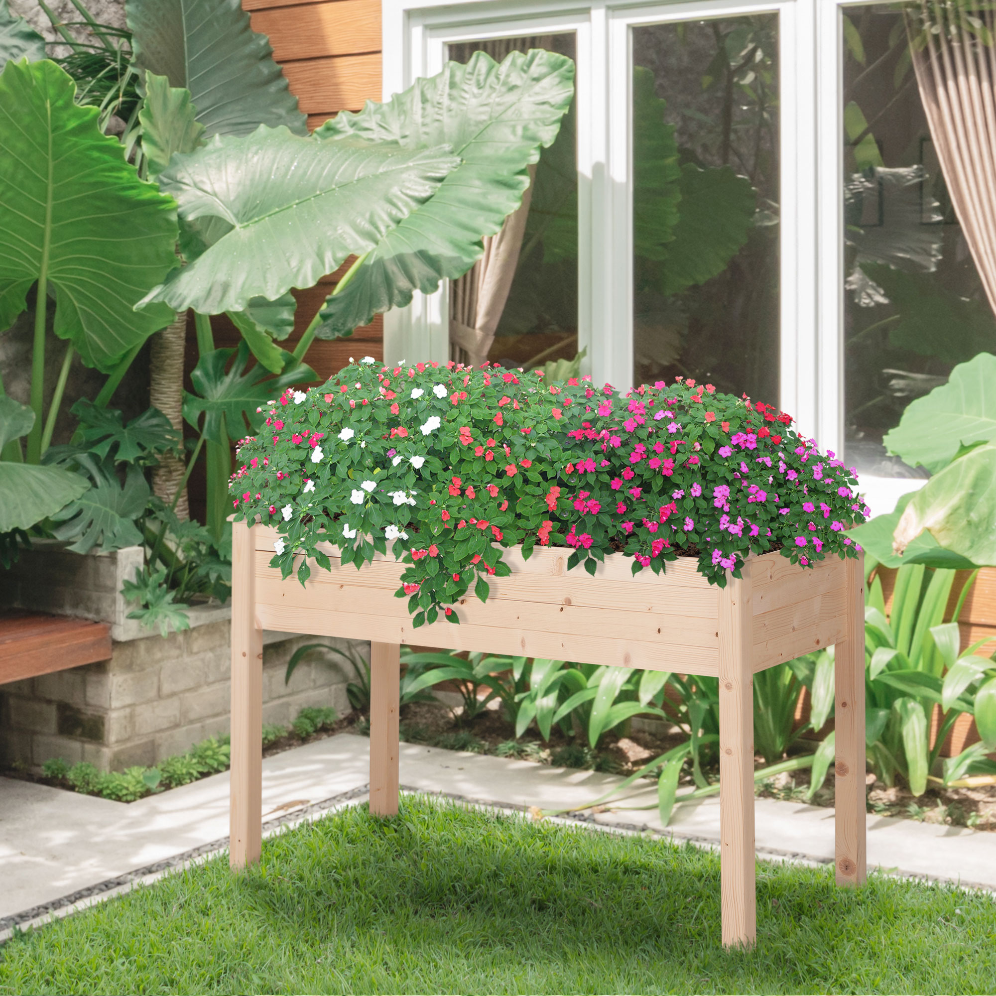 Aiuola rialzata in legno con fiori colorati. Erba verde e fogliame sullo sfondo.