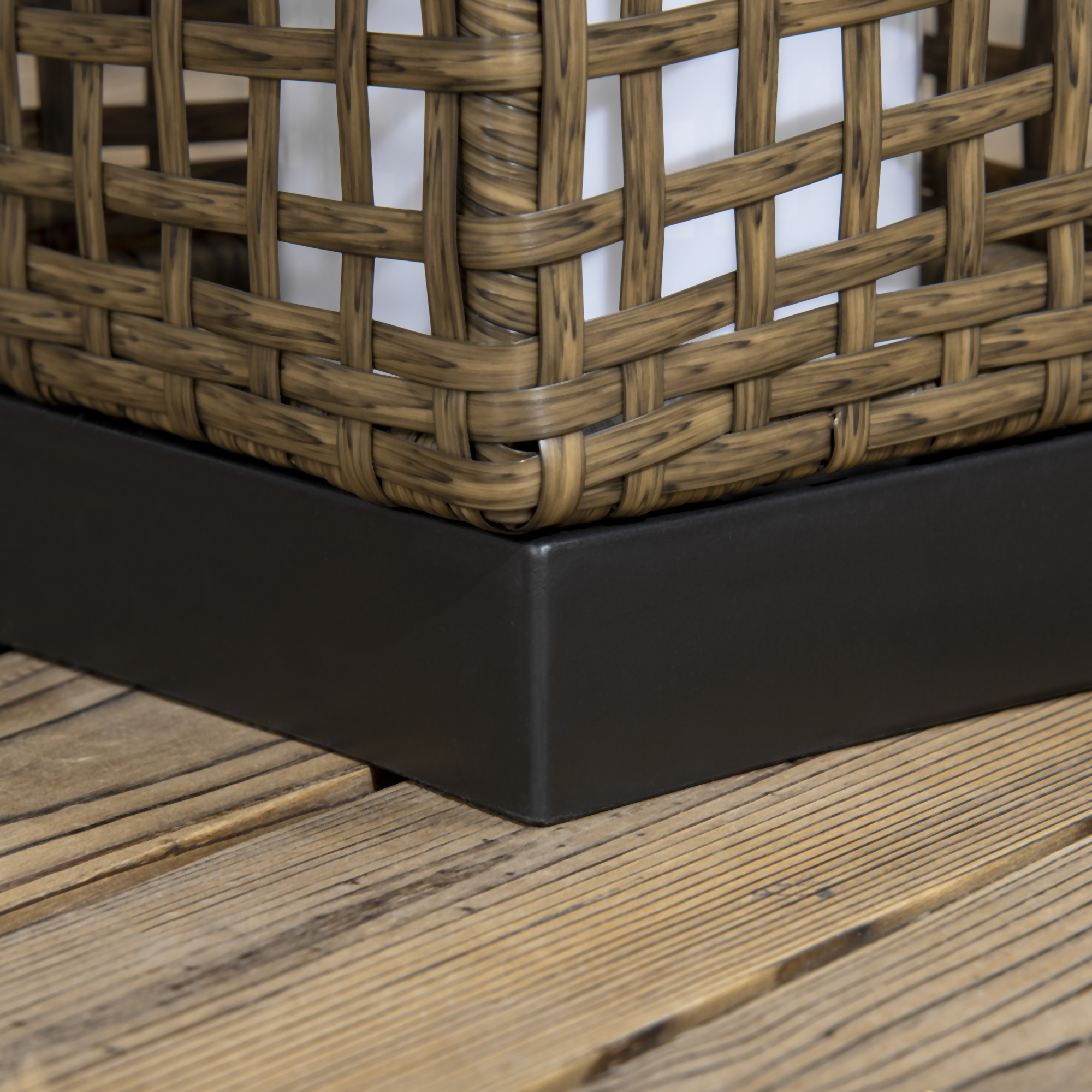 Primo piano della base di un cestino intrecciato. Tessuto marrone e beige su base nera, pavimento in legno.