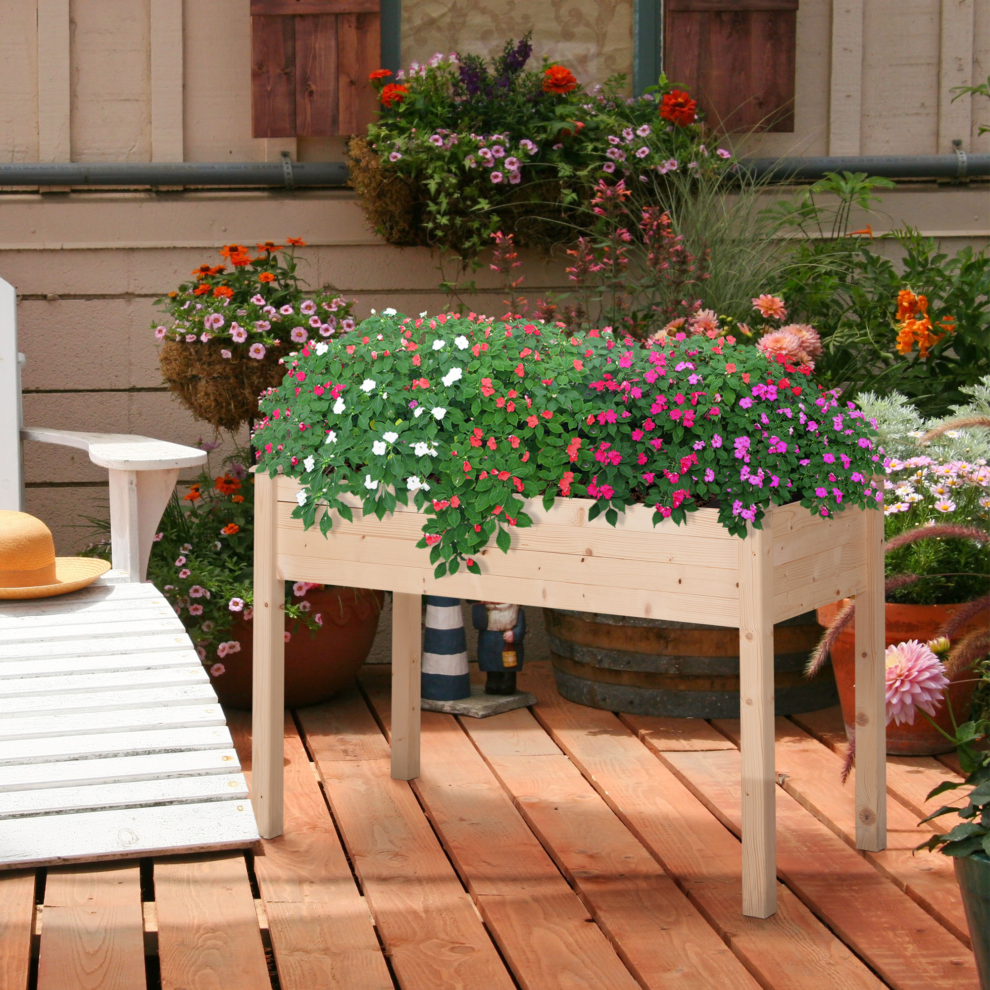 Fioriera in legno con fiori. Sfondo: terrazza in legno con altre piante.