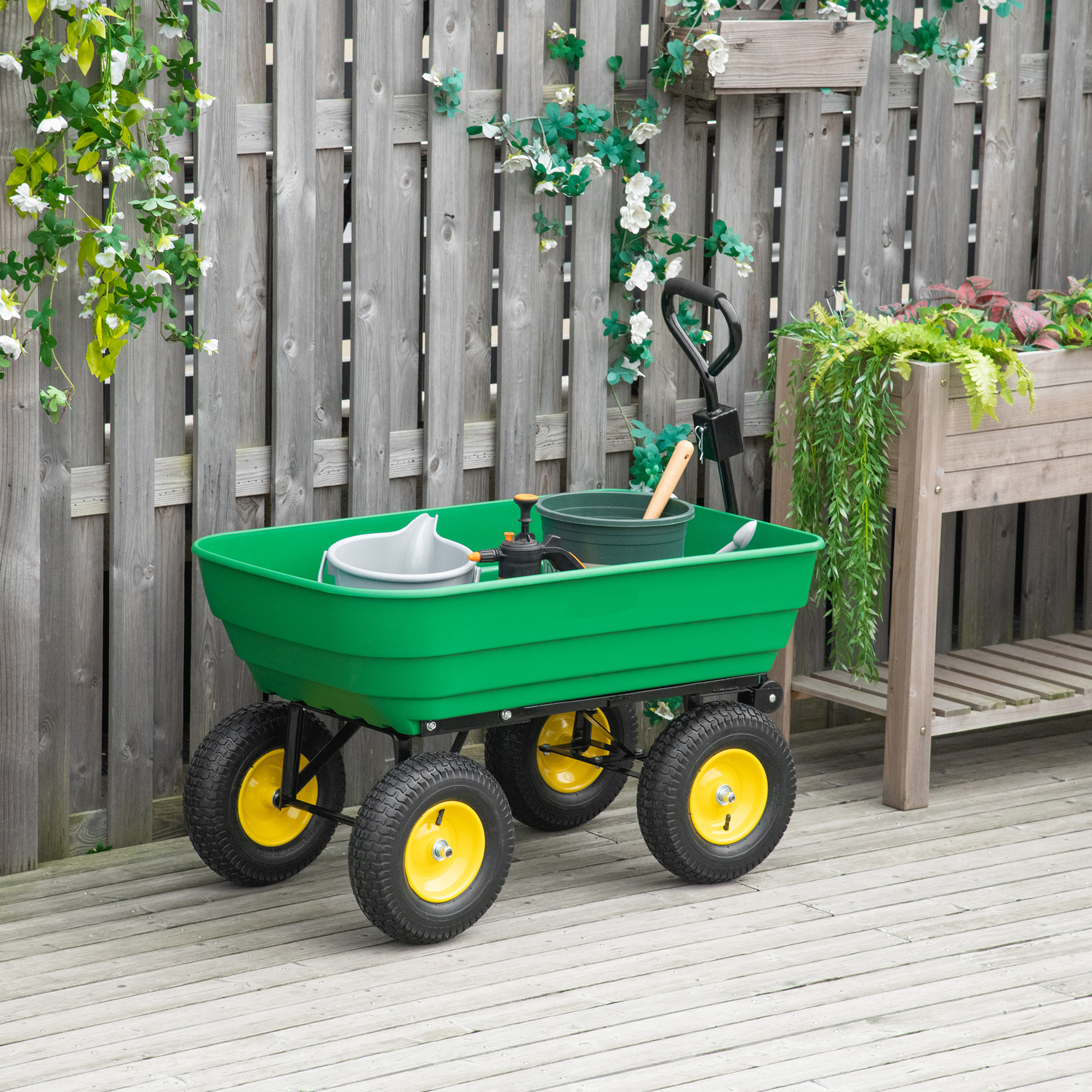 Carrello da giardino verde con ruote gialle su un ponte di legno. Attrezzi e piante all'interno.