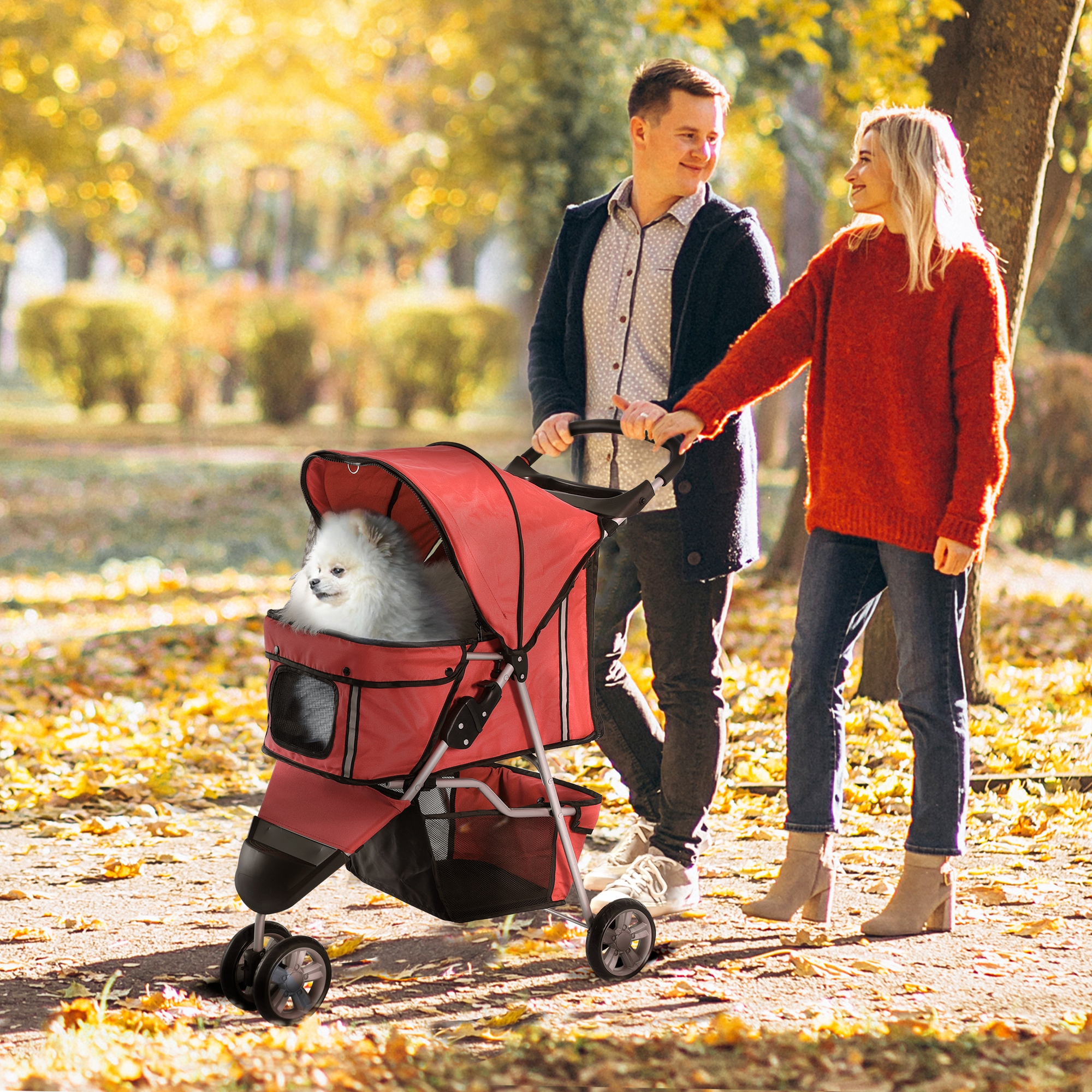 Una coppia che cammina in un parco che spinge un passeggino rosso per cani con un cane bianco dentro. Foglie d'autunno.