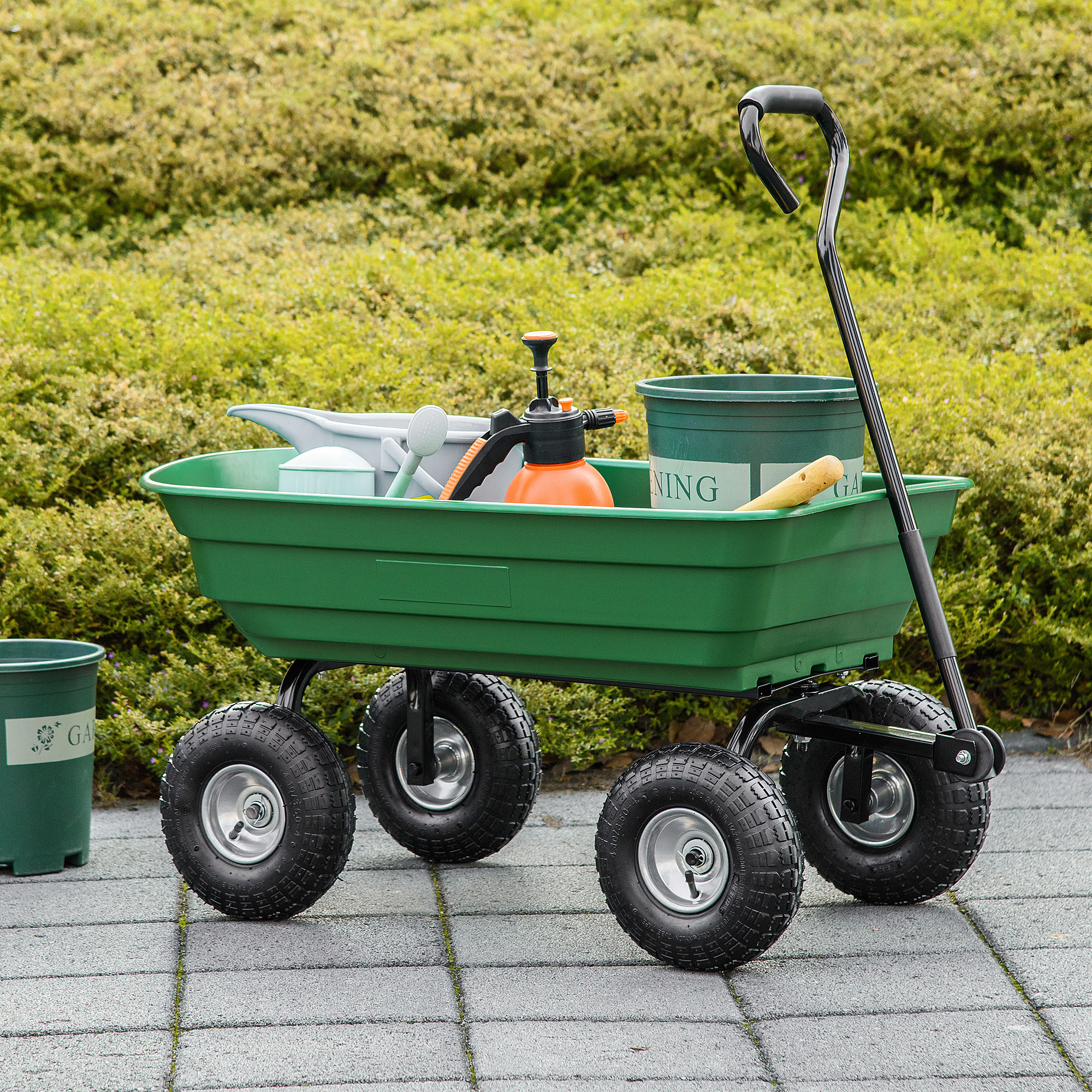 Carrello da giardino verde pieno di attrezzi e forniture da giardinaggio. Ruote nere con cerchi argentati.