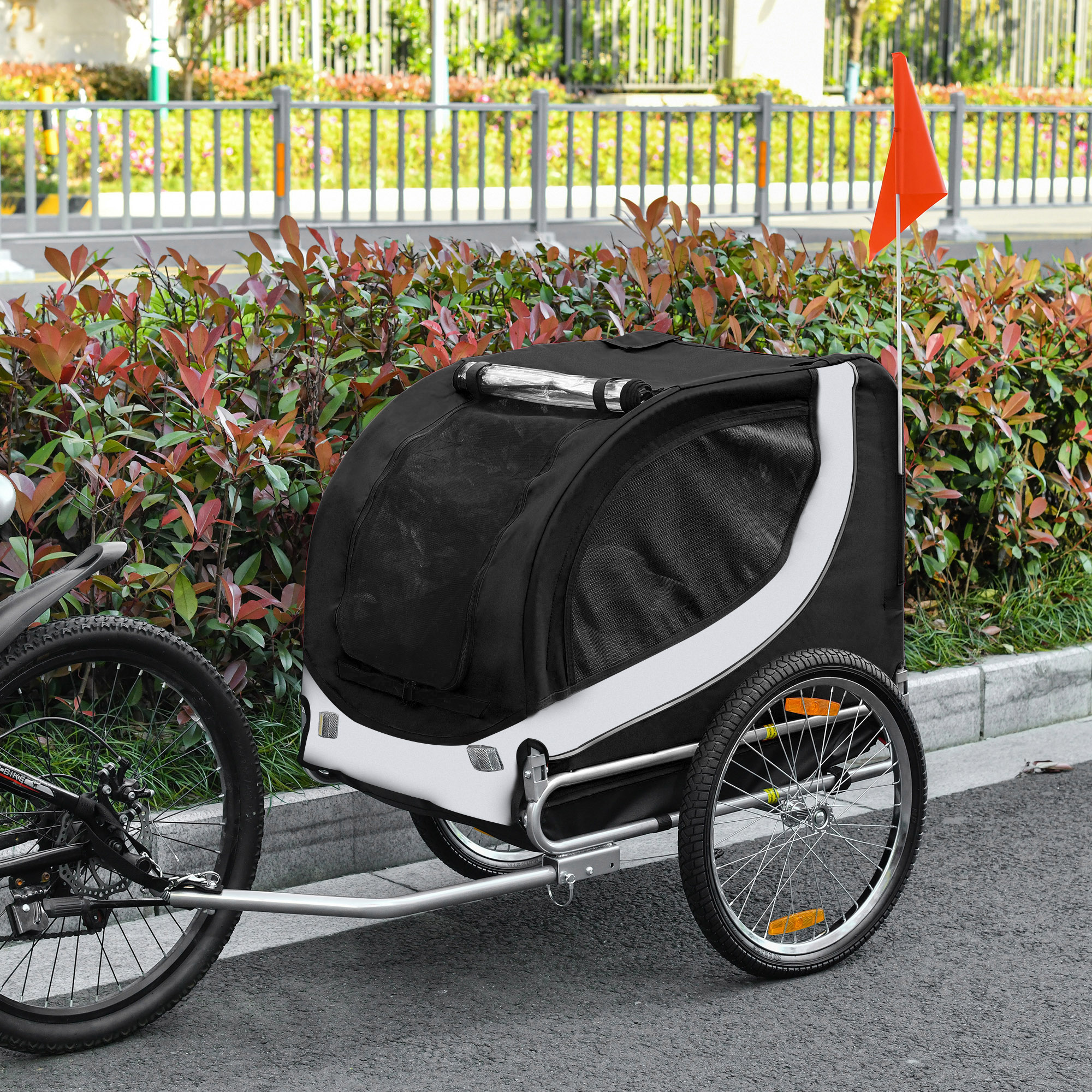 Rimorchio per cani bianco e nero attaccato a una bici. Sventola una bandiera rossa. Il rimorchio è sulla strada.