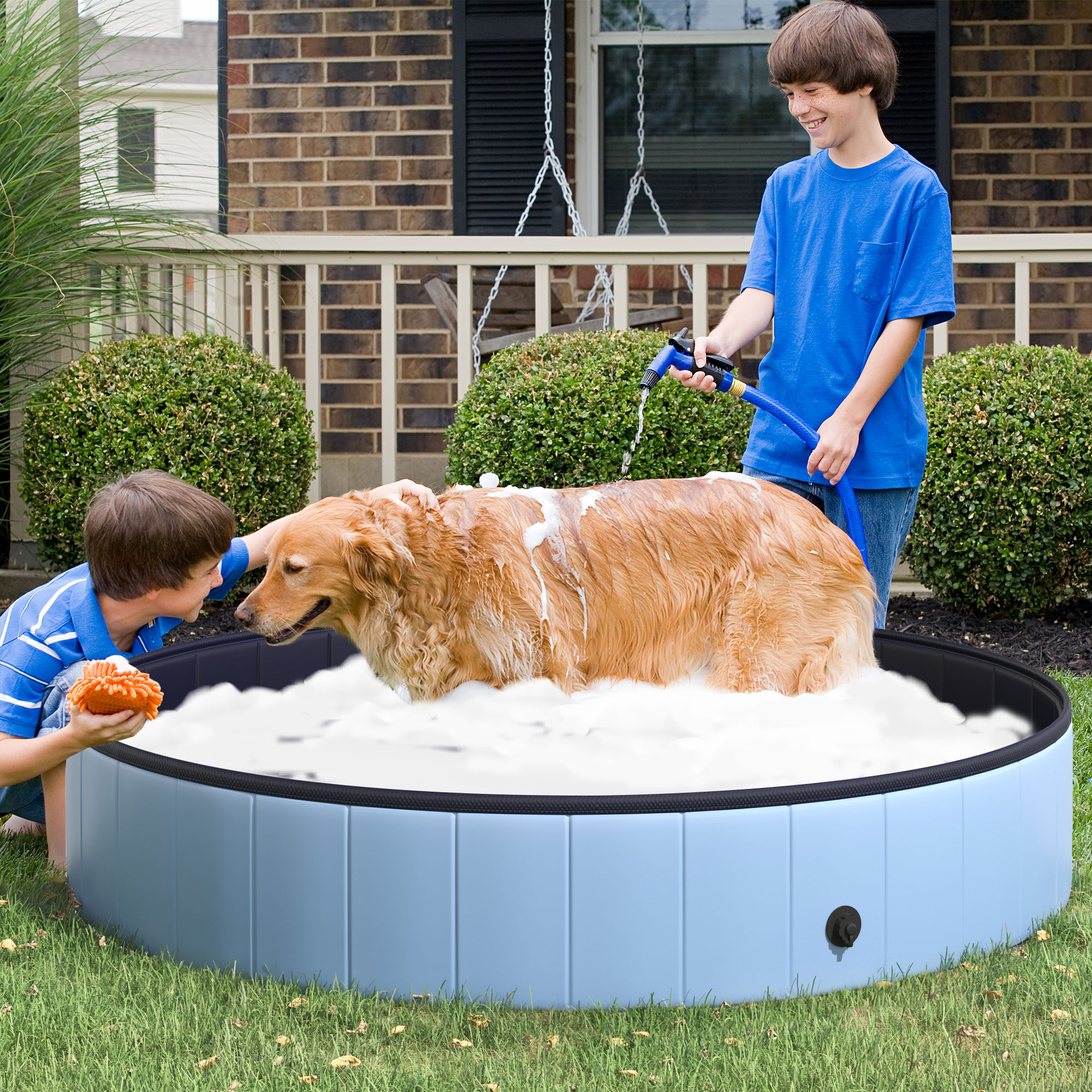 Due ragazzi lavano un golden retriever in una piscina blu piena di schiuma. Un ragazzo ha una spugna.