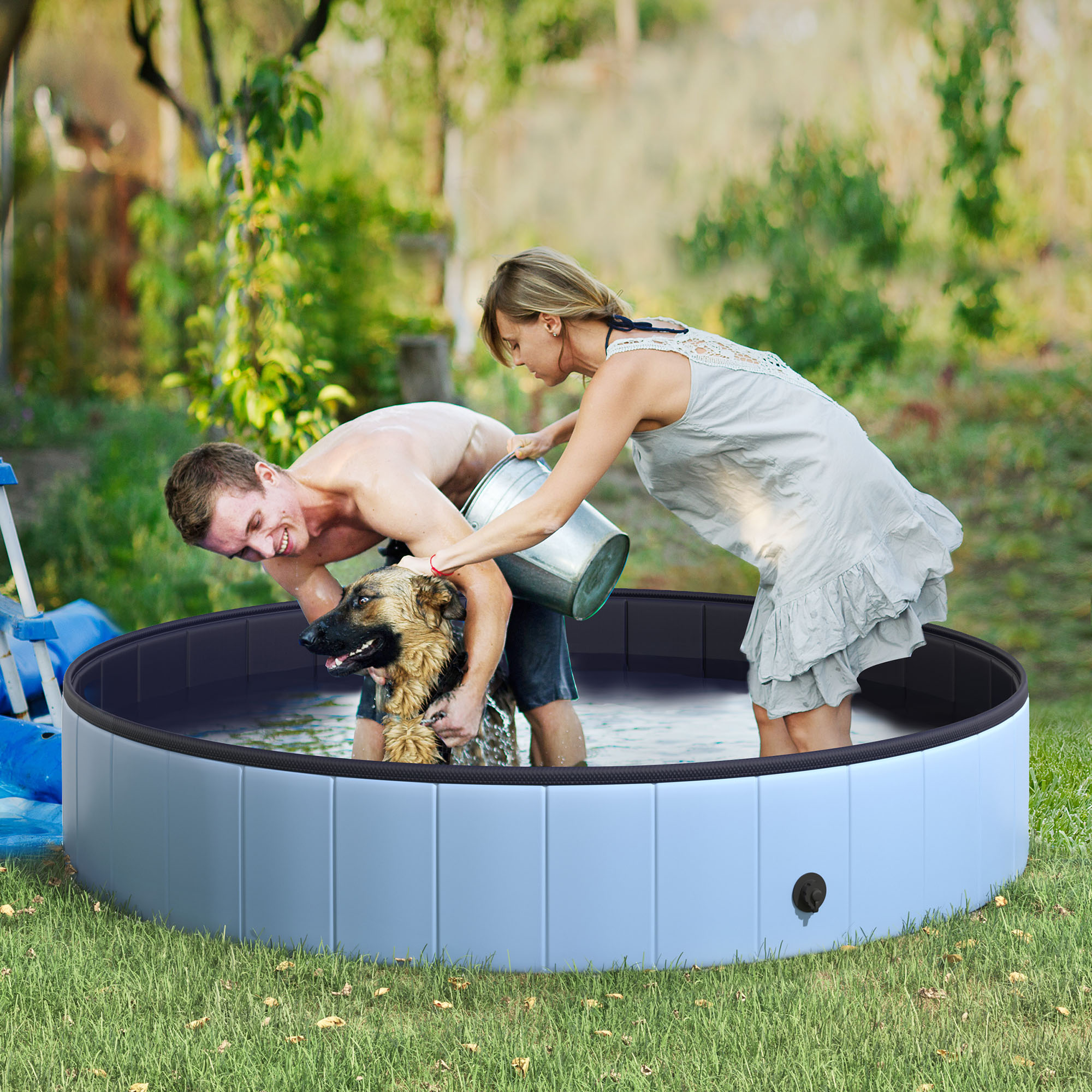 Un uomo e una donna stanno lavando un cane in una piscina blu e nera sull'erba.