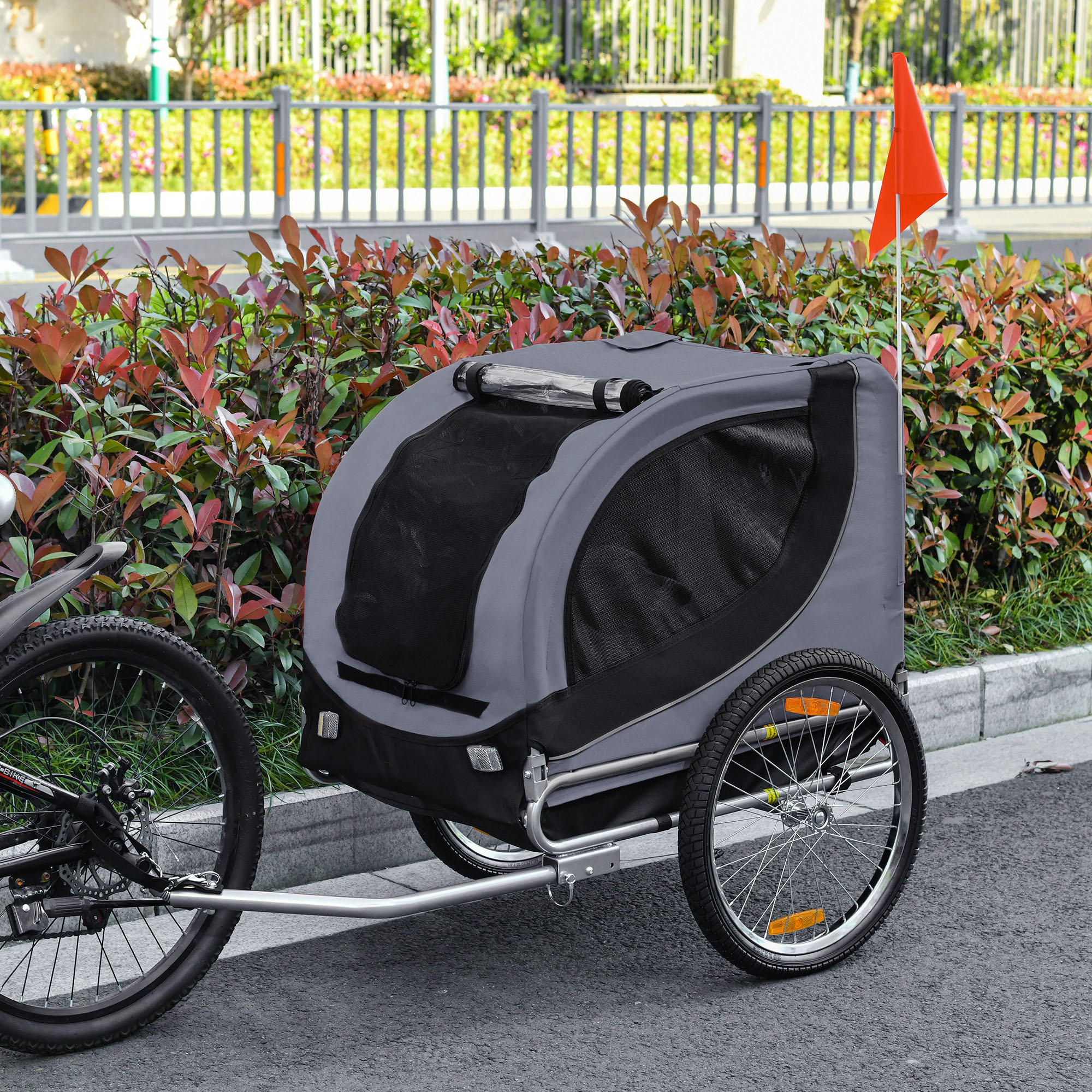 Rimorchio per bici con corpo grigio, dettagli neri e bandiera rossa sul retro.