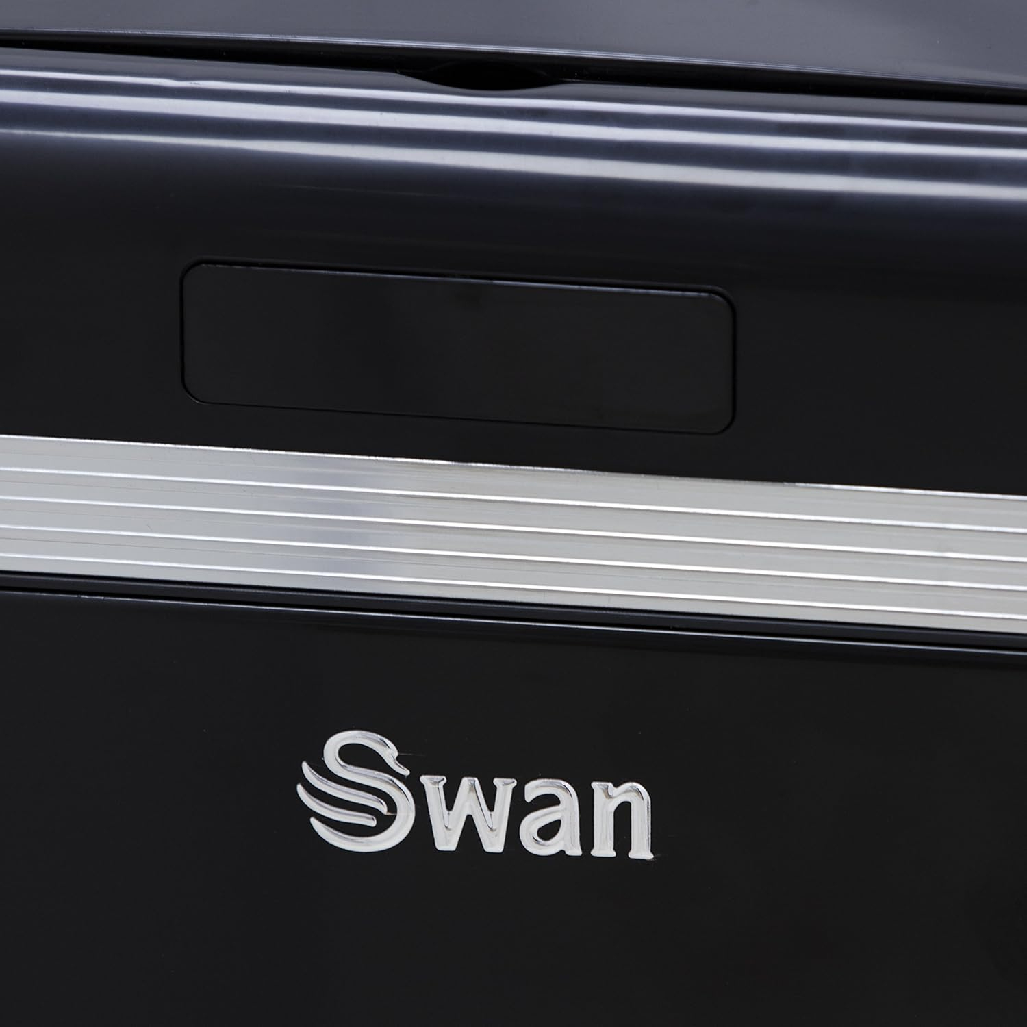 Primer plano de un electrodoméstico negro con el logotipo plateado de Swan. Tiene un asa y una franja plateada.