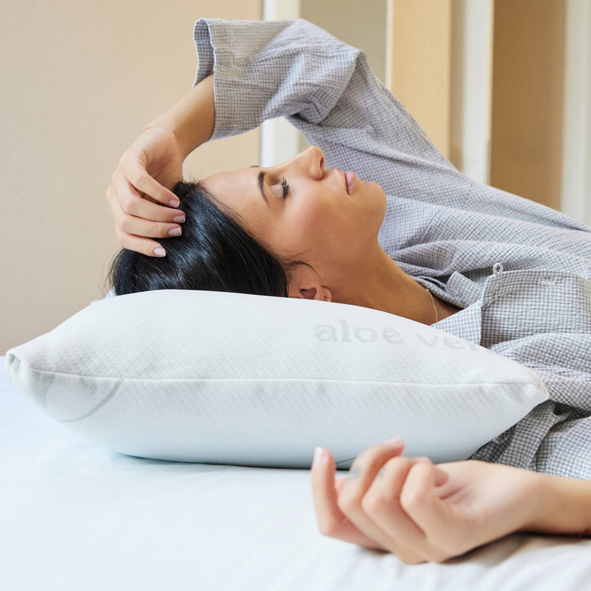 Mujer durmiendo sobre una almohada blanca. La almohada tiene las palabras aloe vera.