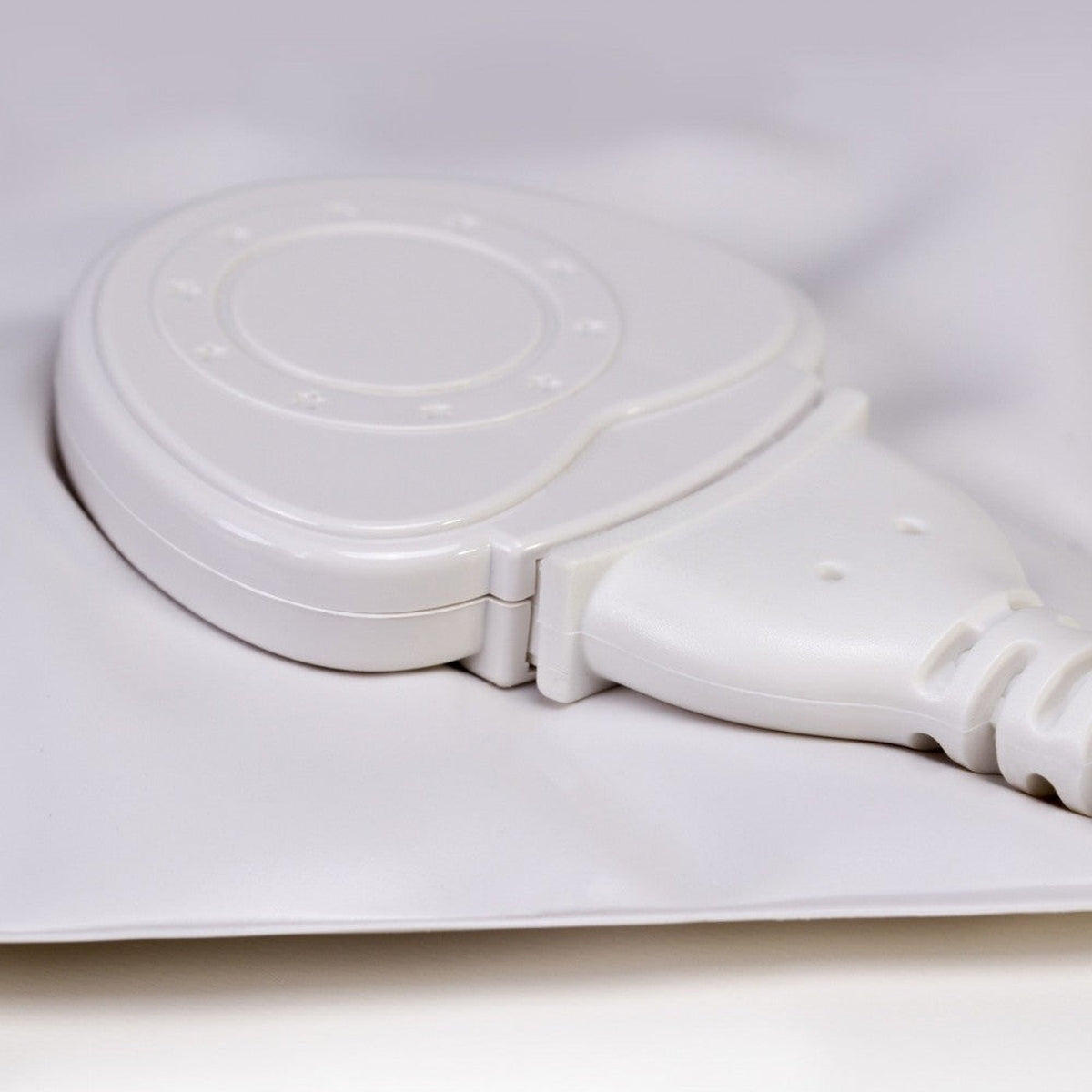 Un dispositivo blanco con un cable conectado. Tiene una parte superior redondeada con detalles circulares y un puerto de conexión.