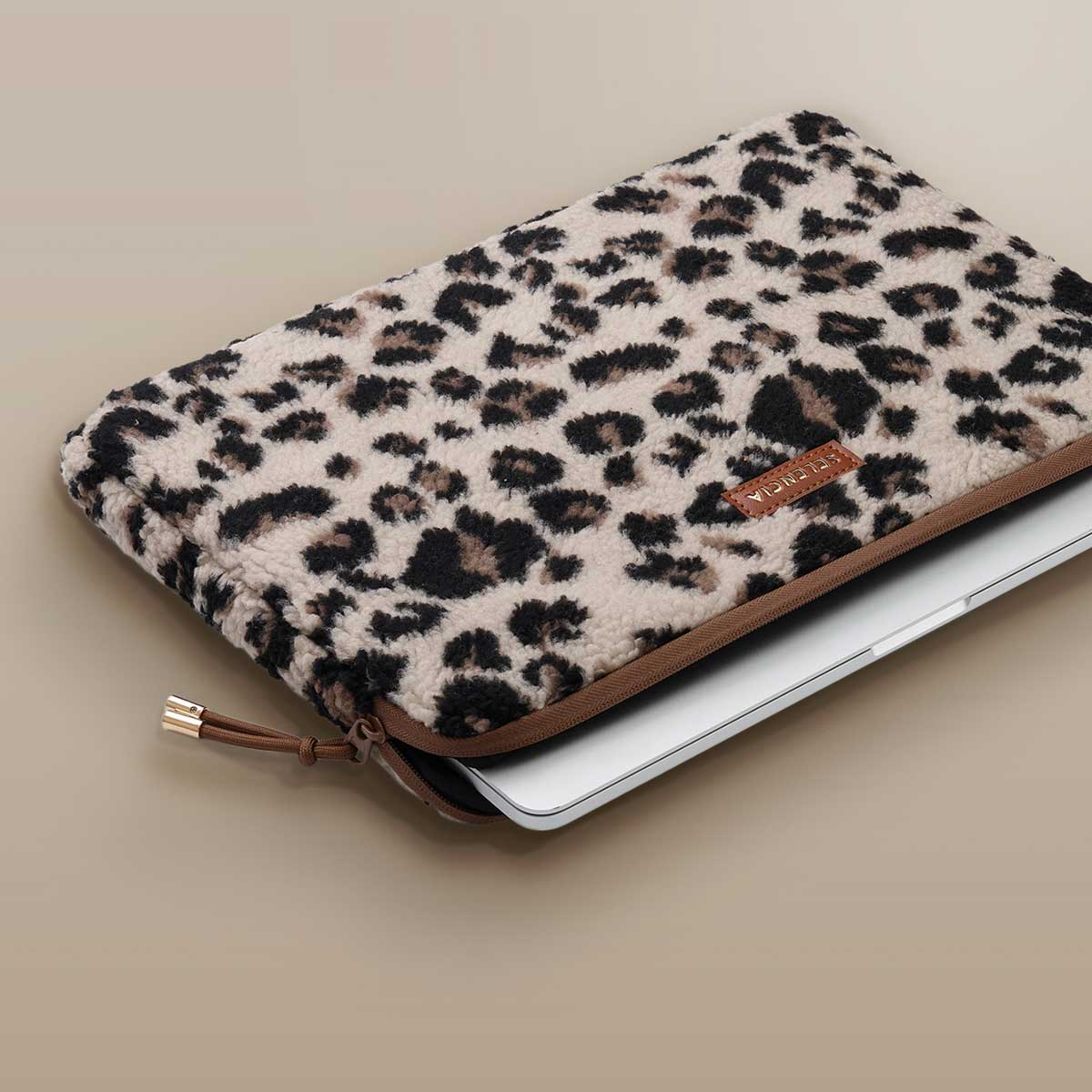 Un portátil en una funda con estampado de leopardo, cerrado. Cremallera en la parte superior. Ribete marrón.