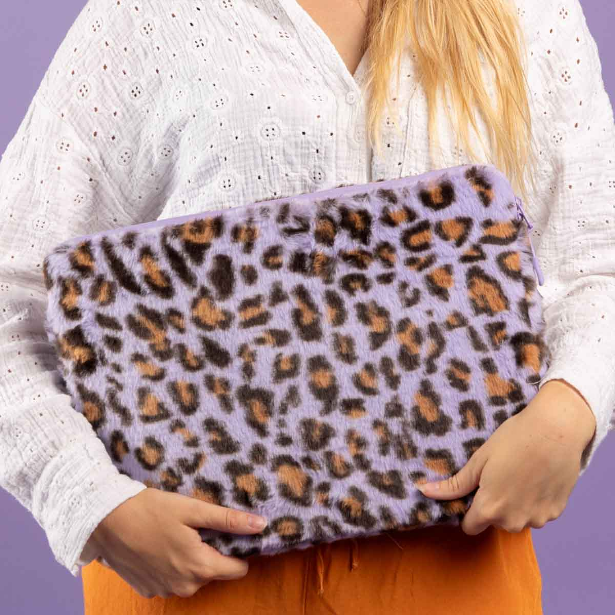 A person holds a laptop sleeve with a purple leopard print pattern.