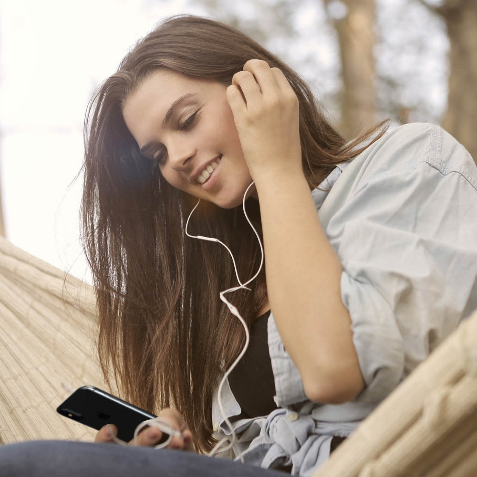 Una mujer escuchando música con auriculares, sosteniendo un teléfono, sonriendo.