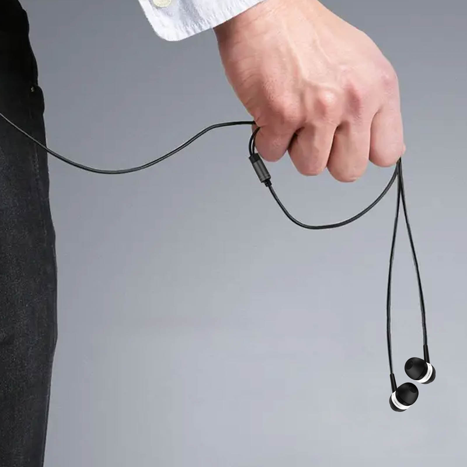 Una mano que sostiene auriculares negros con un cable negro. Los auriculares tienen detalles blancos.