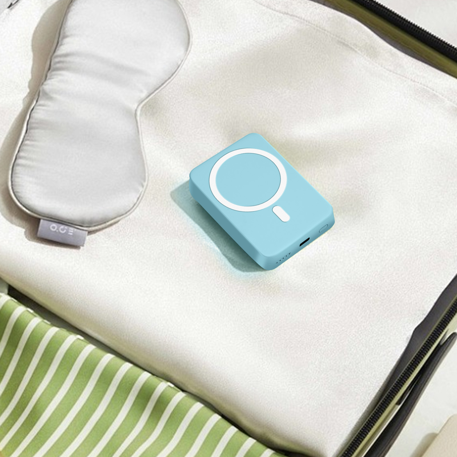 Een blauwe powerbank, oogmasker en spullen in een koffer. De powerbank heeft een witte cirkel.