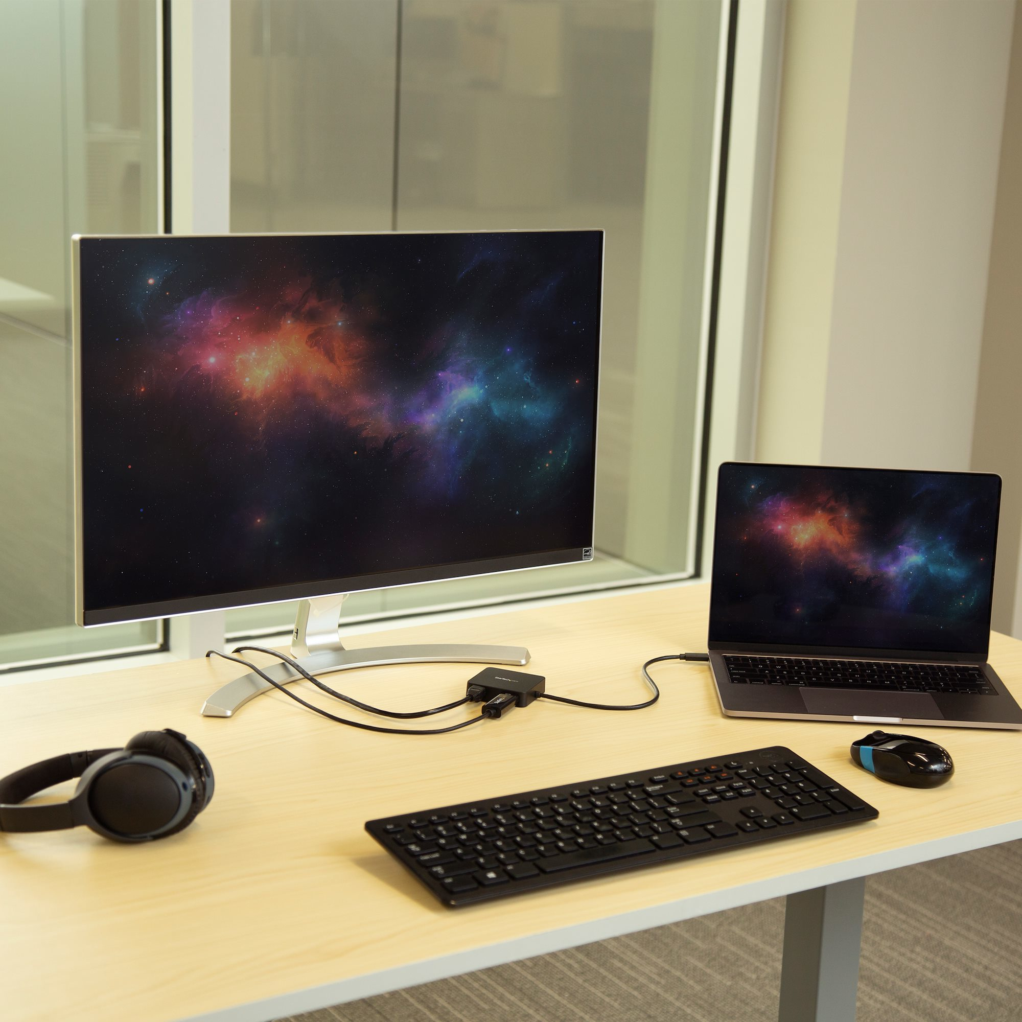 Una scrivania con monitor, laptop, tastiera, mouse e cuffie. Lo schermo mostra colori.