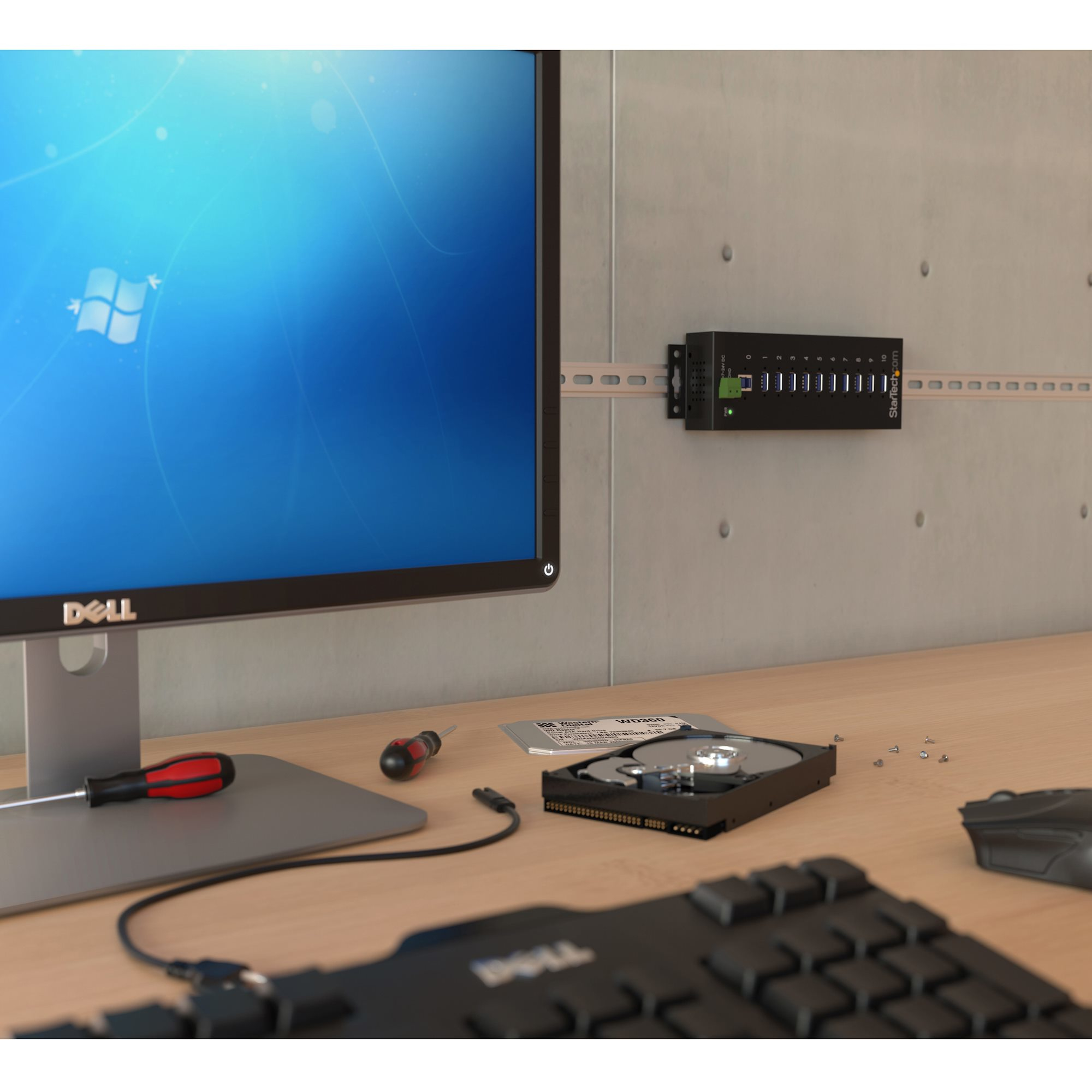 Configuración de computadora con monitor, concentrador USB en la pared, teclado, mouse y disco duro.