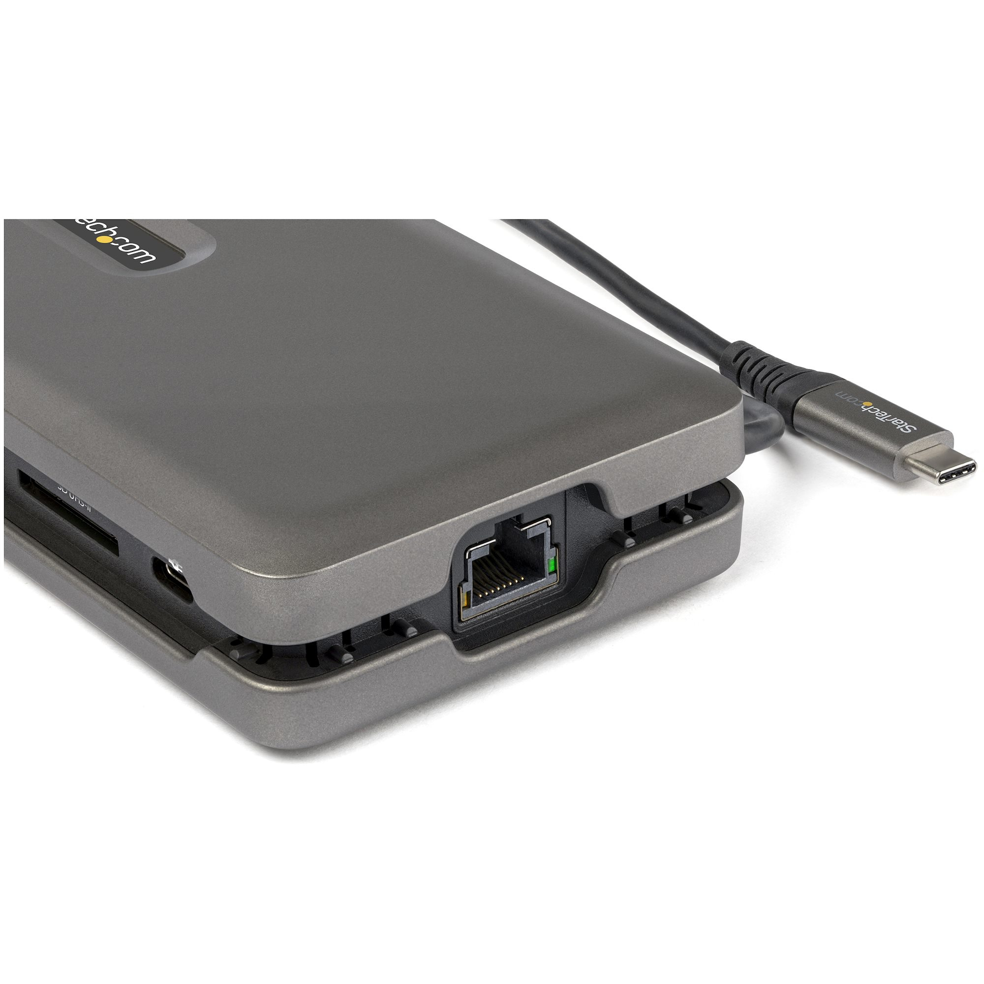 Estación de acoplamiento gris con varios puertos y un cable negro con conector USB-C. Fondo blanco.