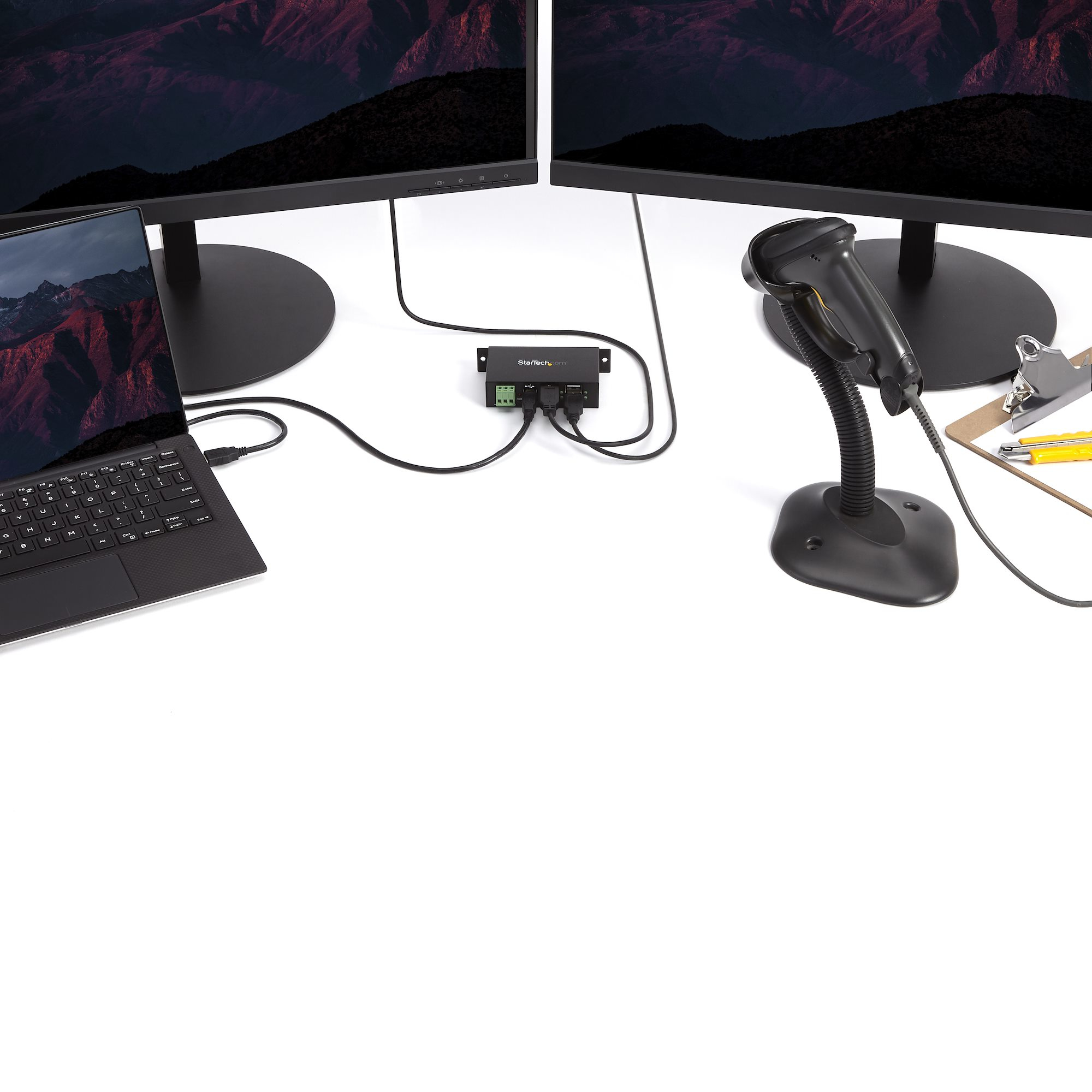 Due monitor, un laptop e uno scanner di codici a barre collegati a un hub.
