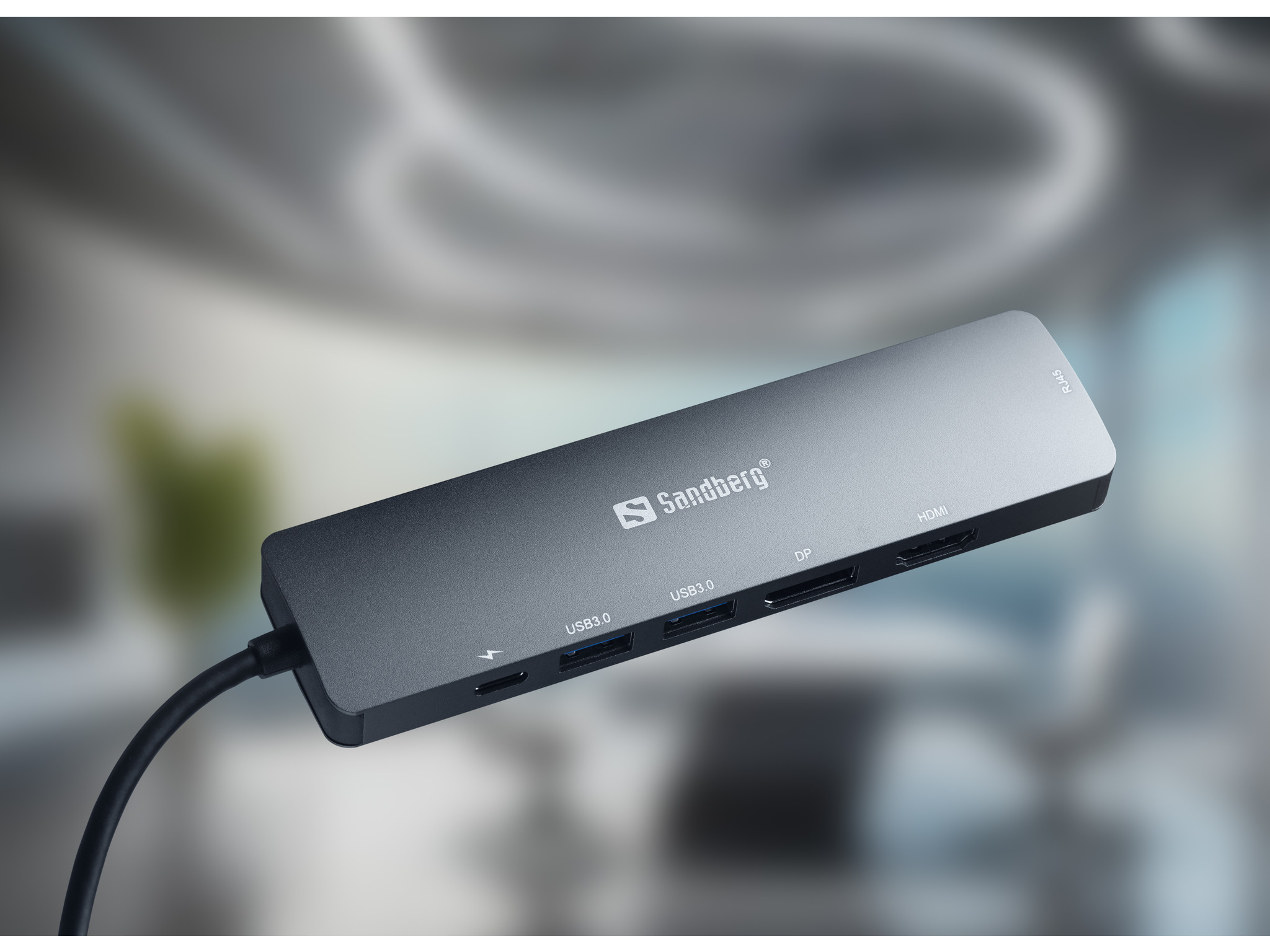 Ein dunkelgrauer USB-Hub mit mehreren Anschlüssen, darunter USB 3.0, DP und HDMI, vor verschwommenem Hintergrund.