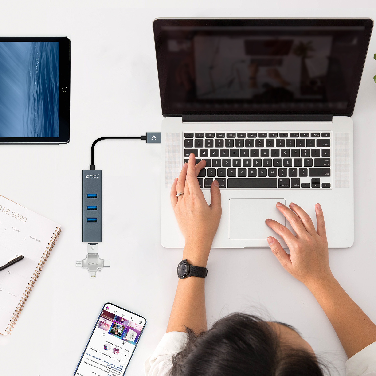 Una persona usa un laptop collegato a un hub USB, con un tablet e un telefono nelle vicinanze.