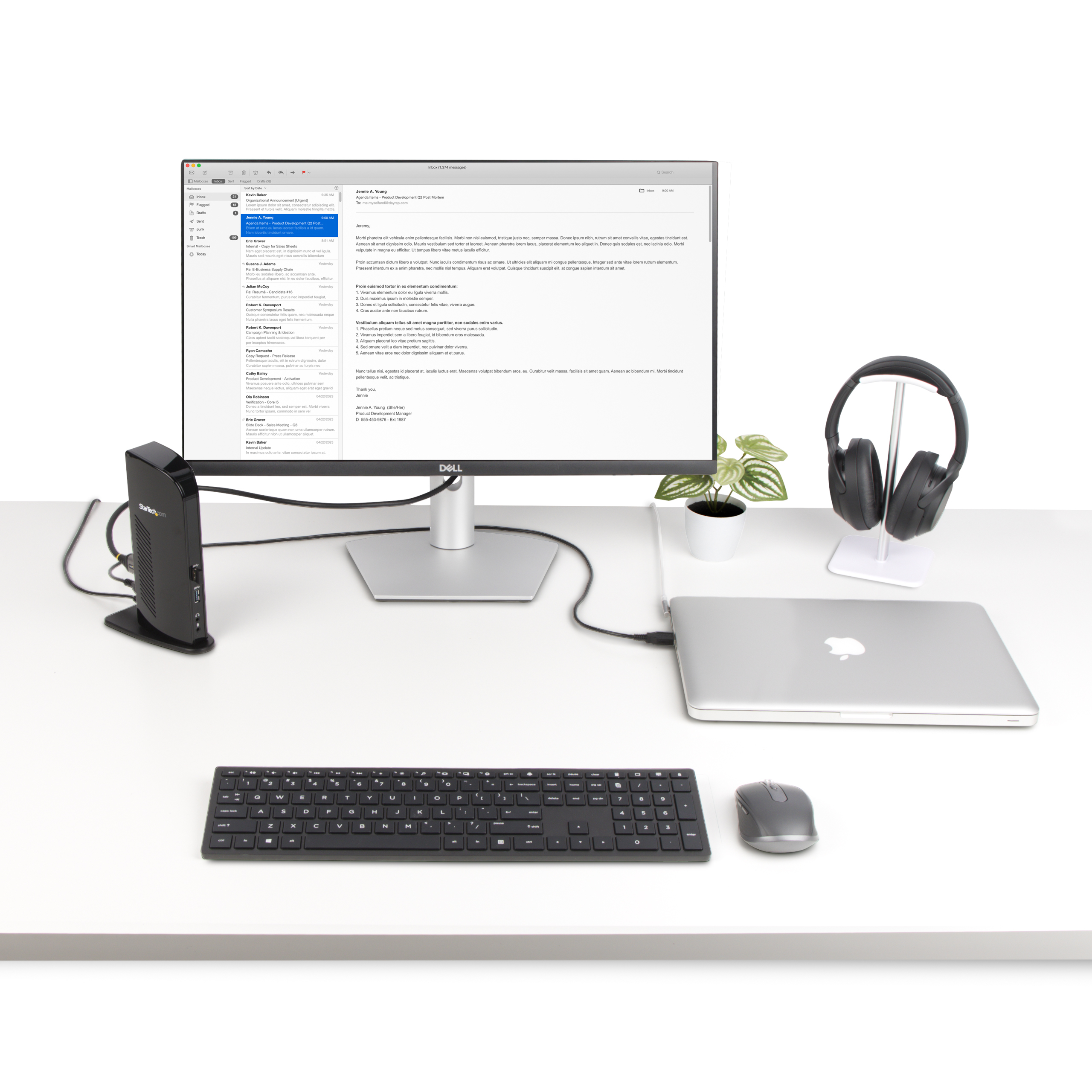 Configuración de escritorio con monitor, portátil, teclado, ratón y auriculares. Adaptador negro visible.
