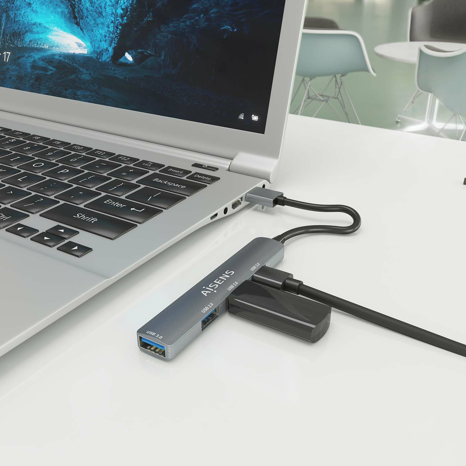 Laptop collegato a un hub USB argentato con più porte e un dispositivo USB nero.