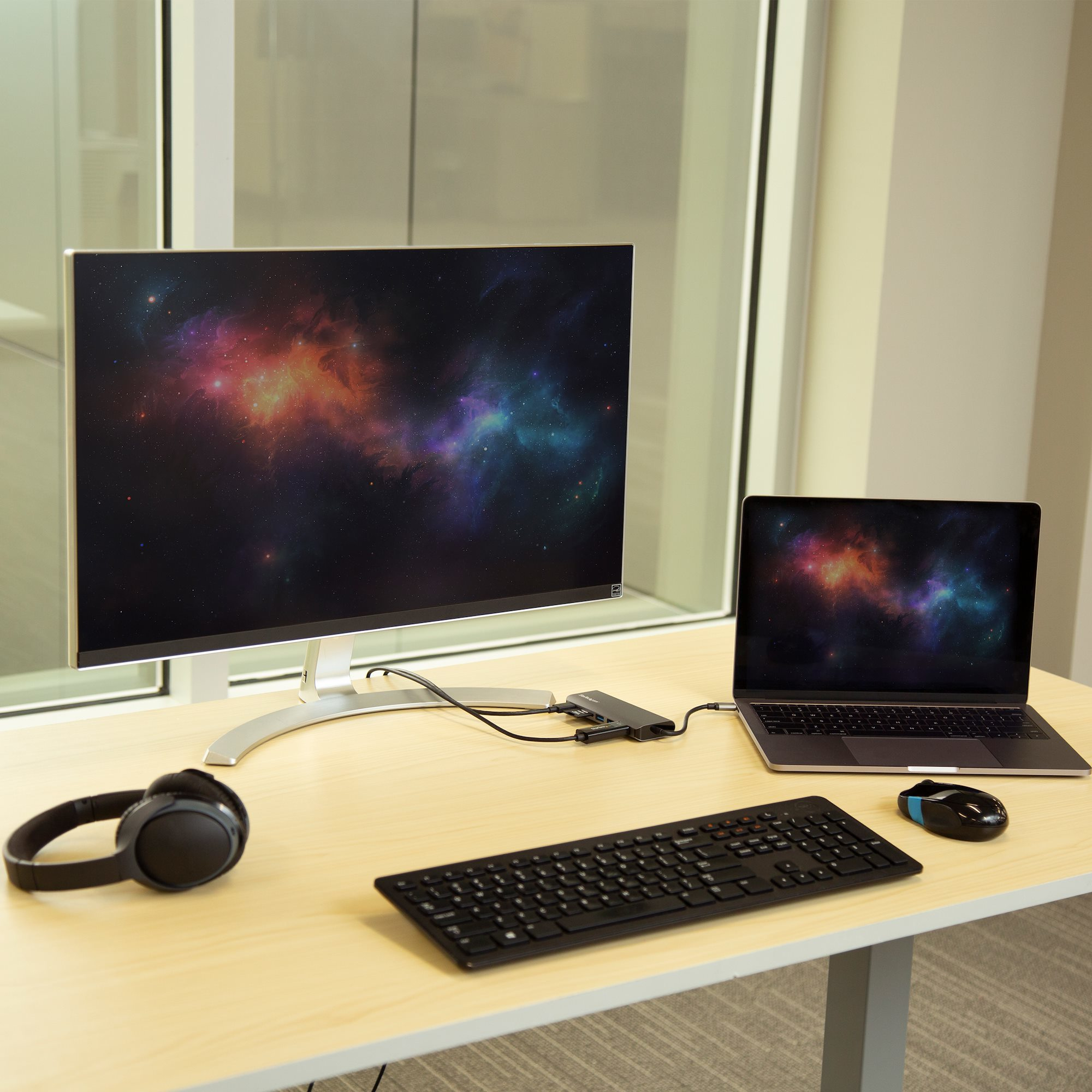 Uno spazio di lavoro con un monitor che mostra un'immagine della galassia, un laptop e altri accessori.