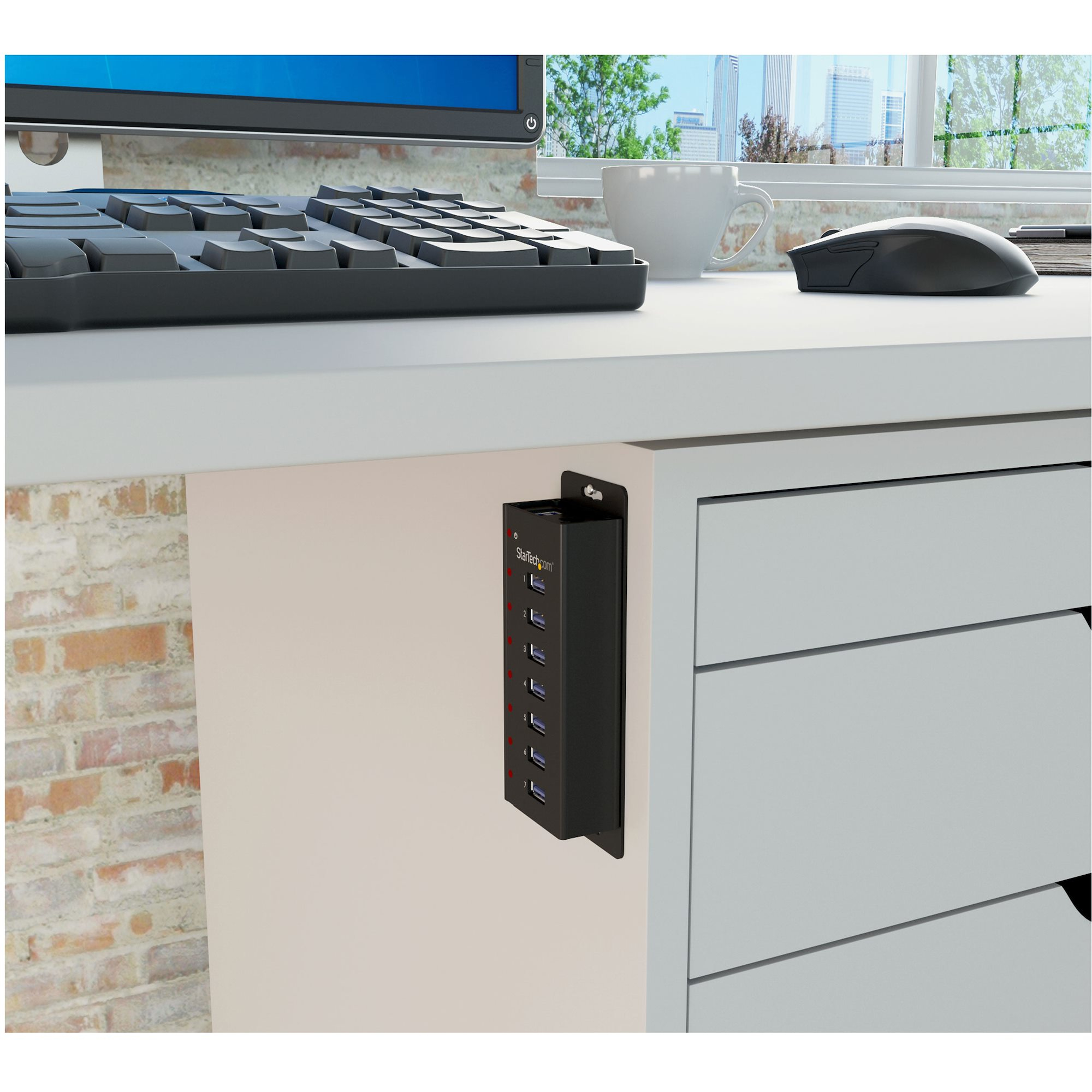 Un hub USB nero montato su una scrivania, con cavi, mouse e tastiera visibili.