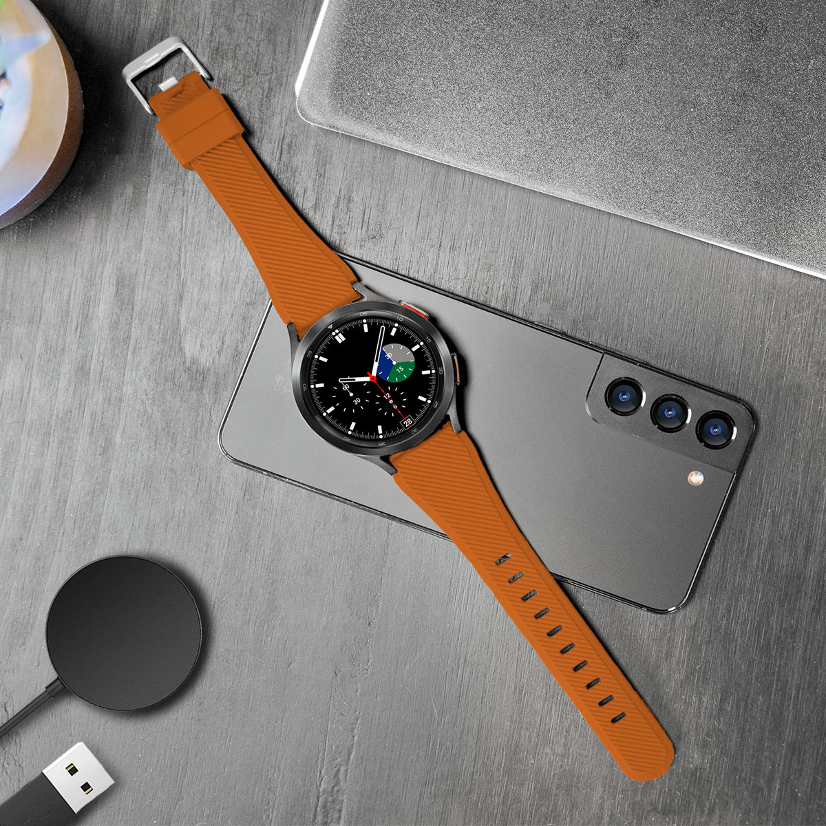 Smartwatch auf einem Telefon, Power-Pad und USB-Kabel auf Holzoberfläche.