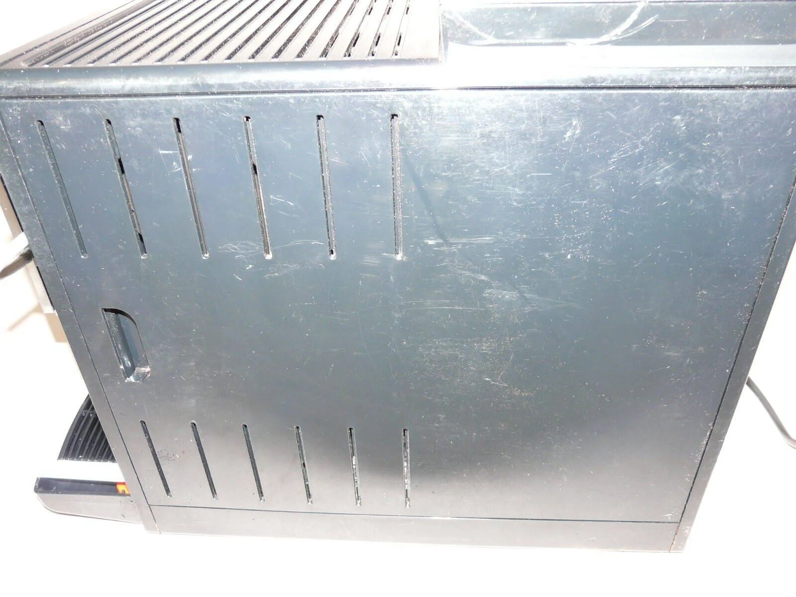 Widok z boku czarnego ekspresu do kawy z zadrapaniami, otwory wentylacyjne.